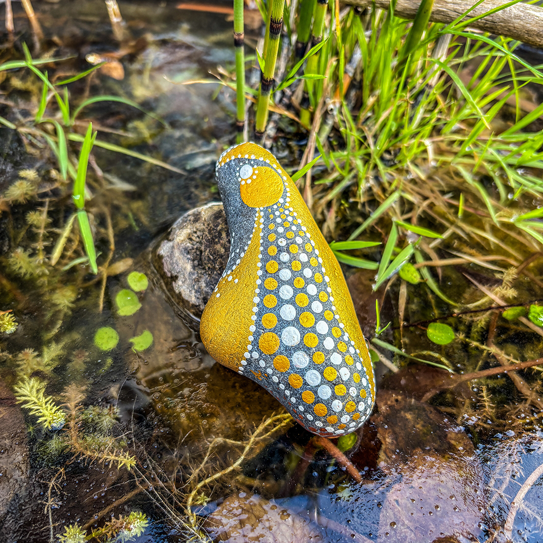 Mit einem Engel bemalter Stein vor Gras auf Eisfläche