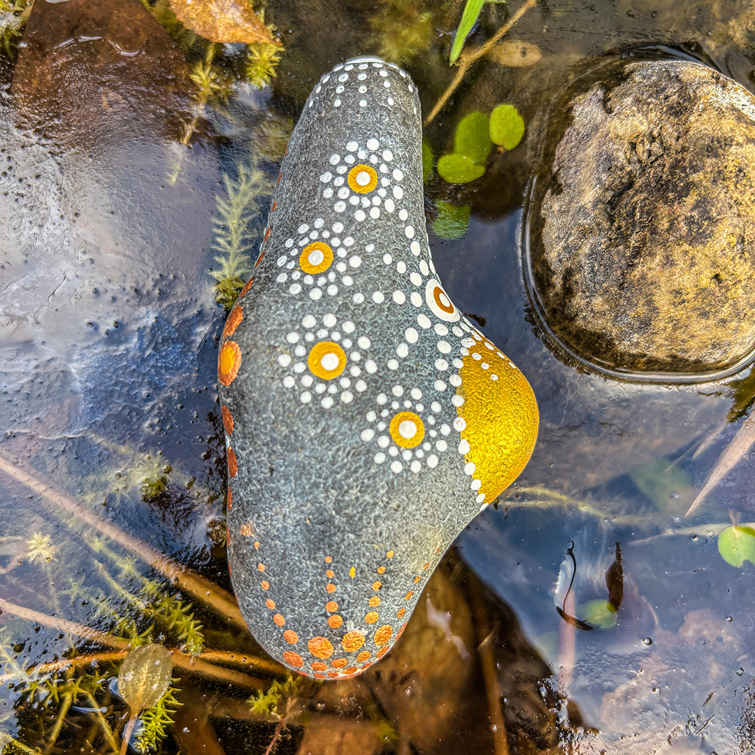Ein in Dot Painting Technik bemalter Stein auf Eisfläche