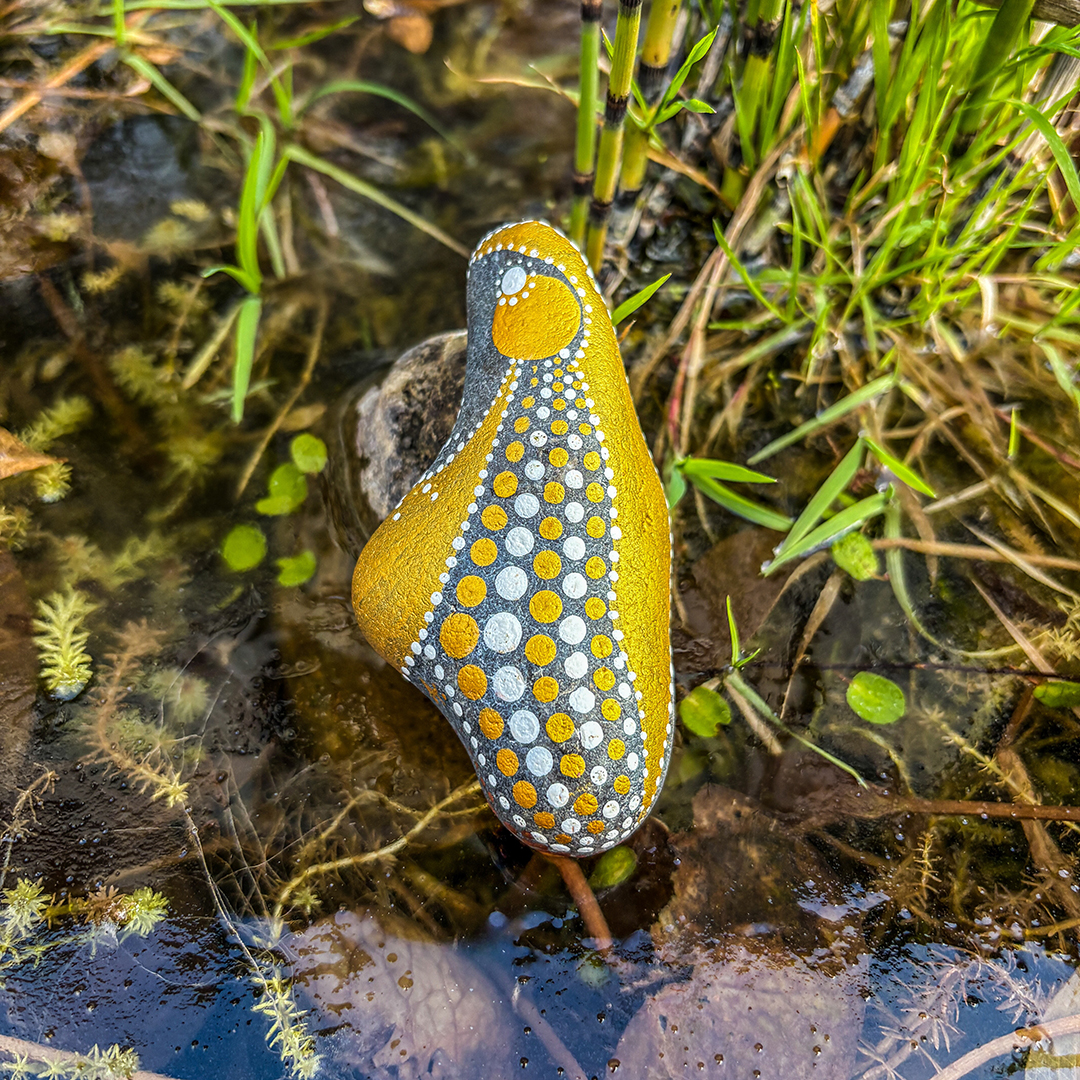 Mit einem Engel bemalter Stein vor Gras auf Eisfläche