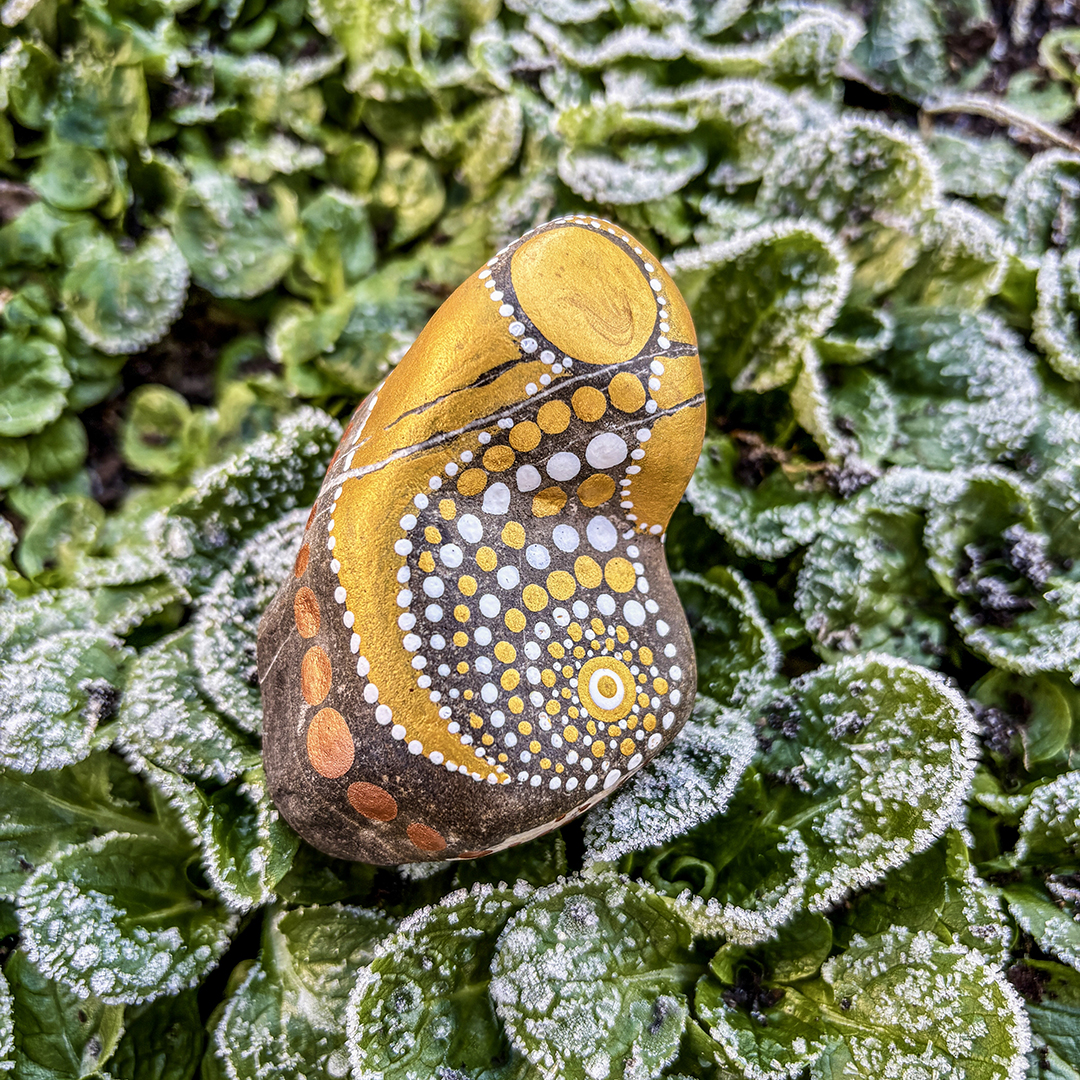 Bemalter Stein mit Engel auf frostigen Blättern liegend