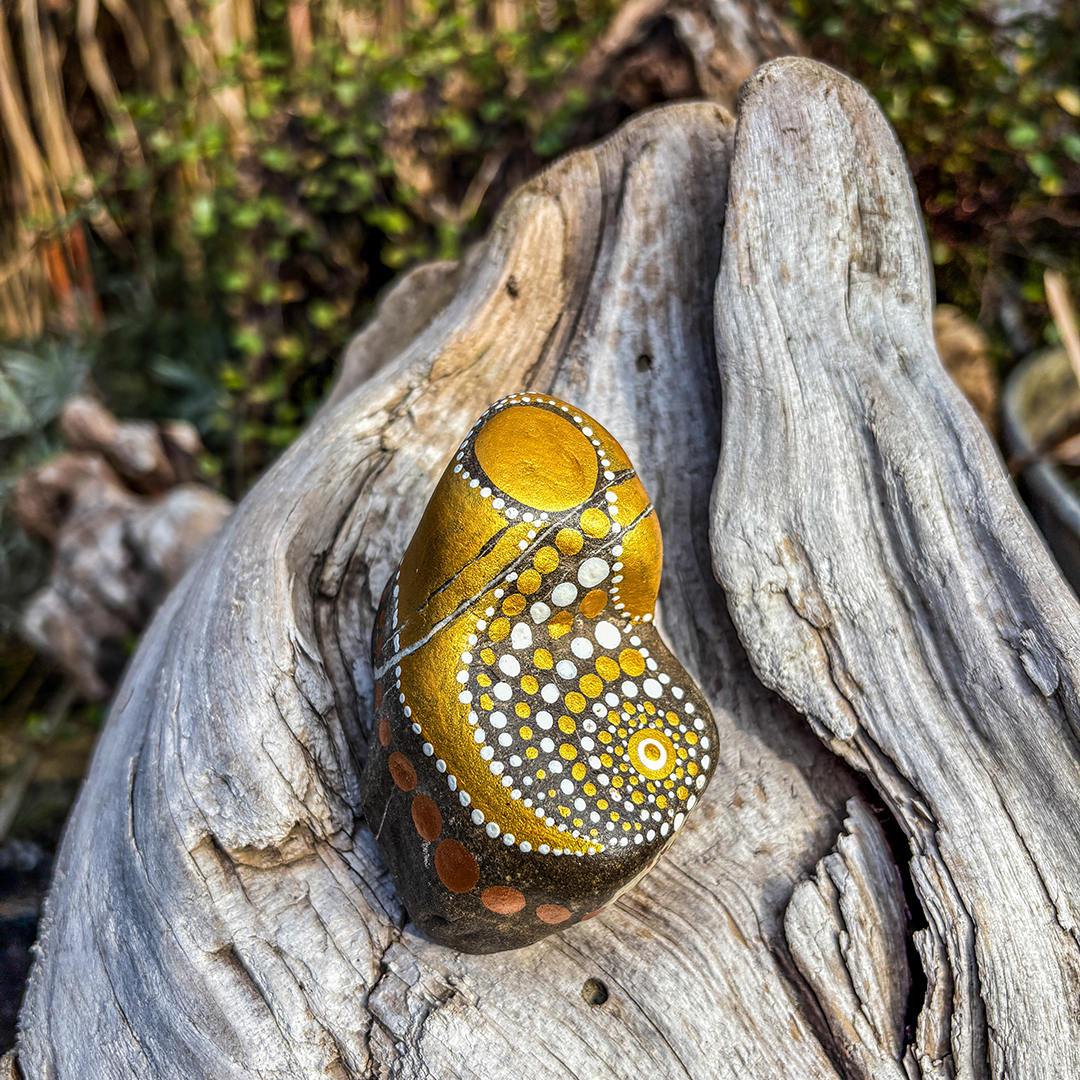 Bemalter Stein mit Engel auf Holz liegend