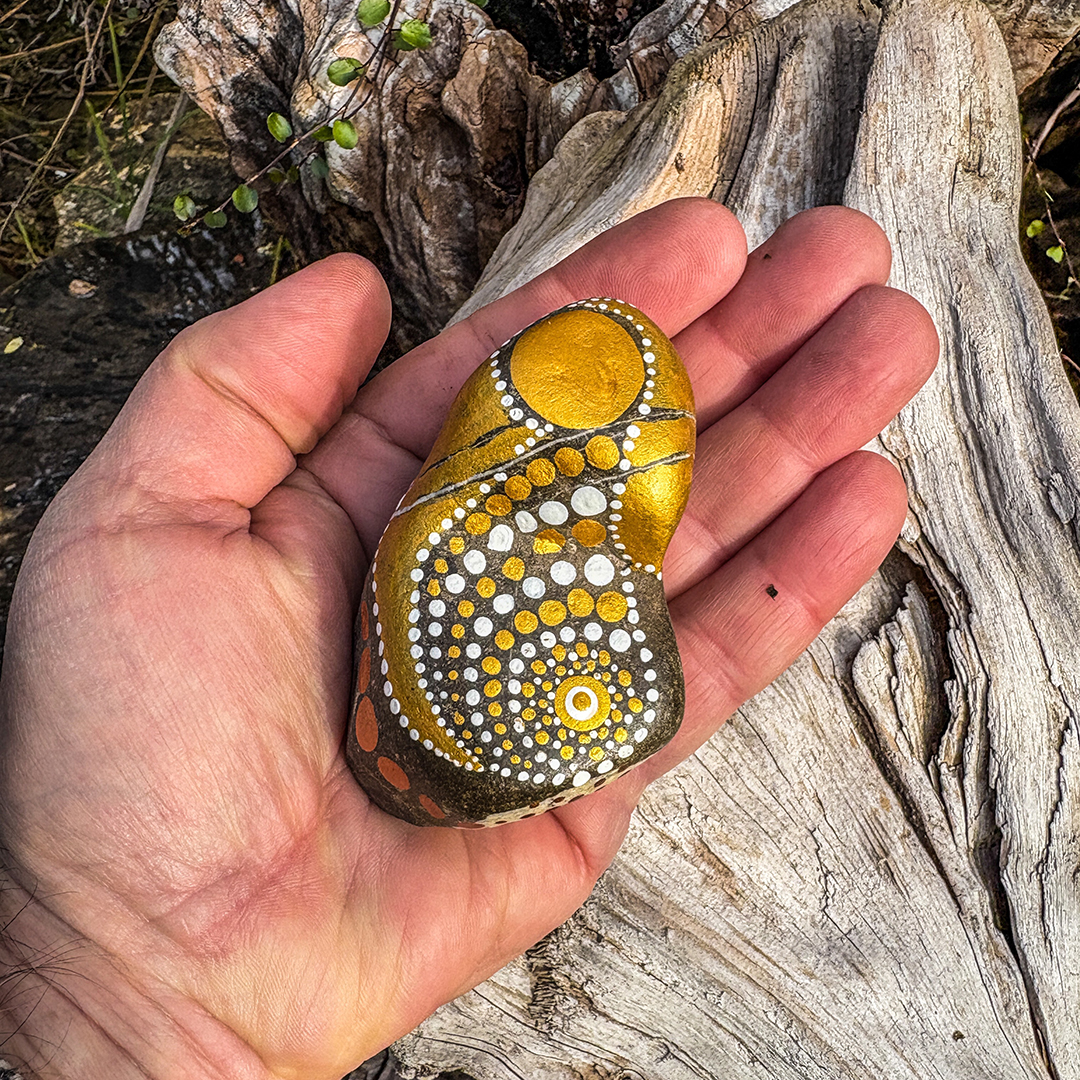 Bemalter Stein mit Engel auf Hand liegend vor Holz