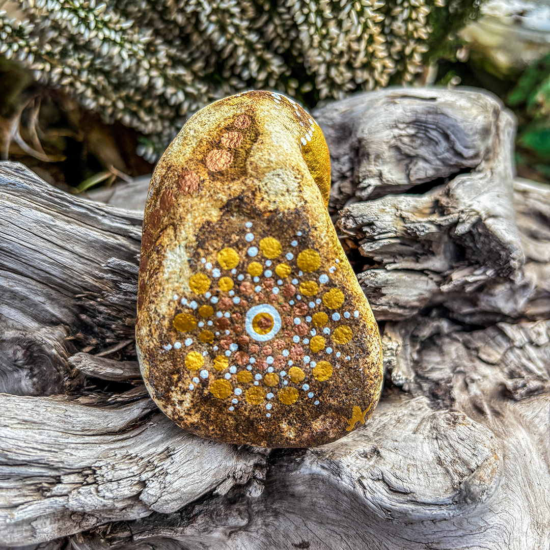 in Dot Painting Technik bemalter Stein auf Holz vor weißer Erikapflanze