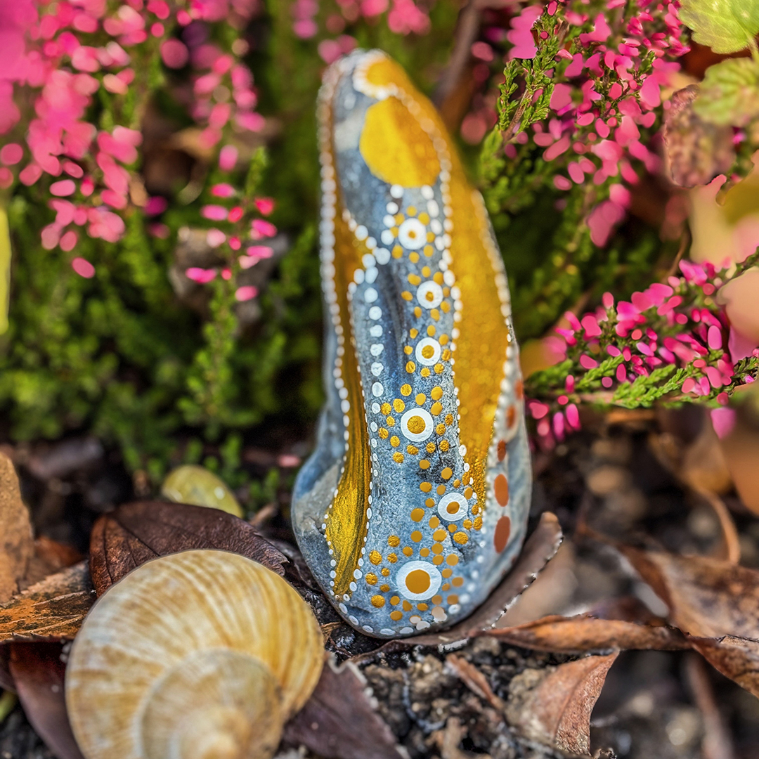 Bemalter Stein mit Engel vor roter Erikapflanze neben Schneckenhaus