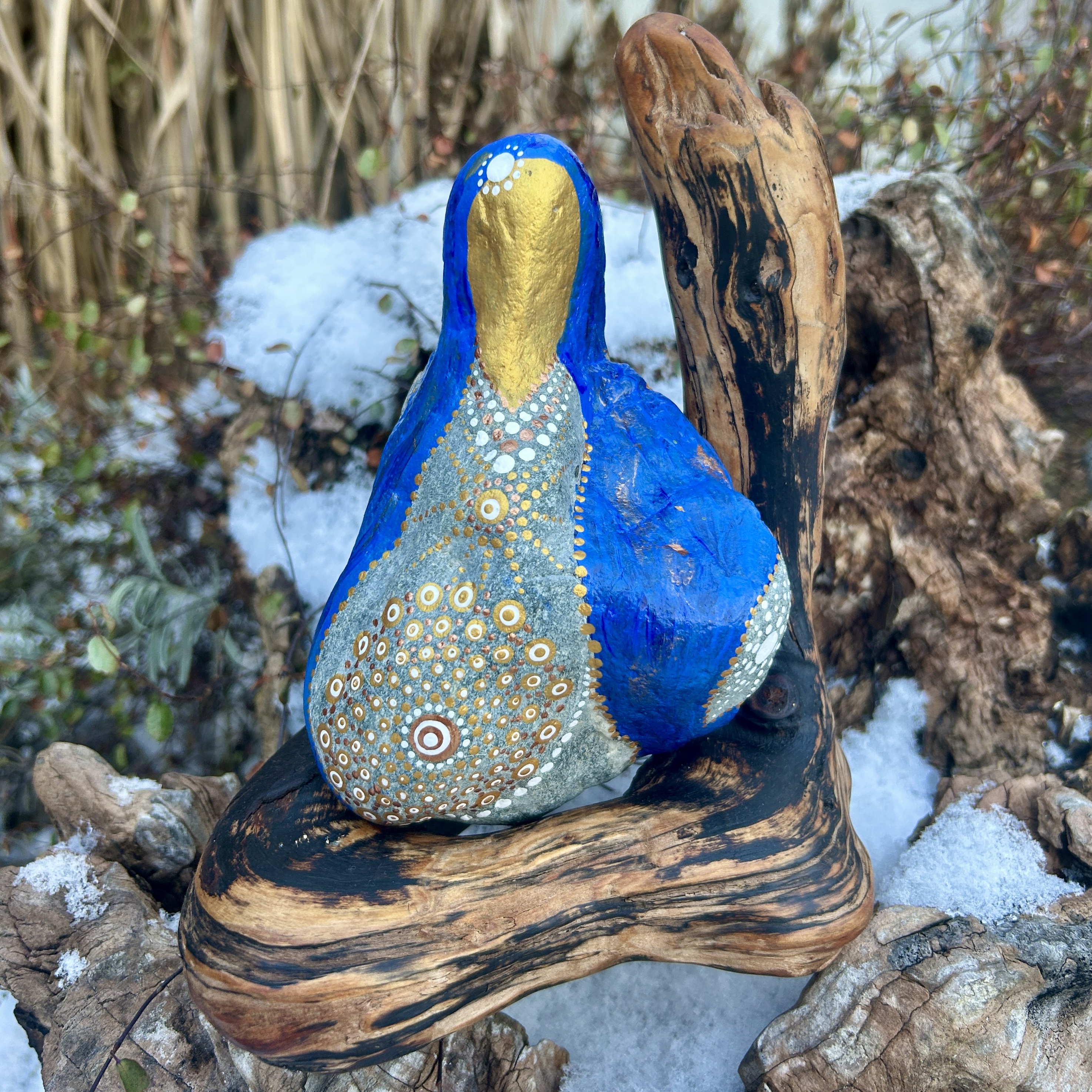 Stein in blau und gold in der Gestalt von Mutter Maria bemalt auf Treibholz stehend