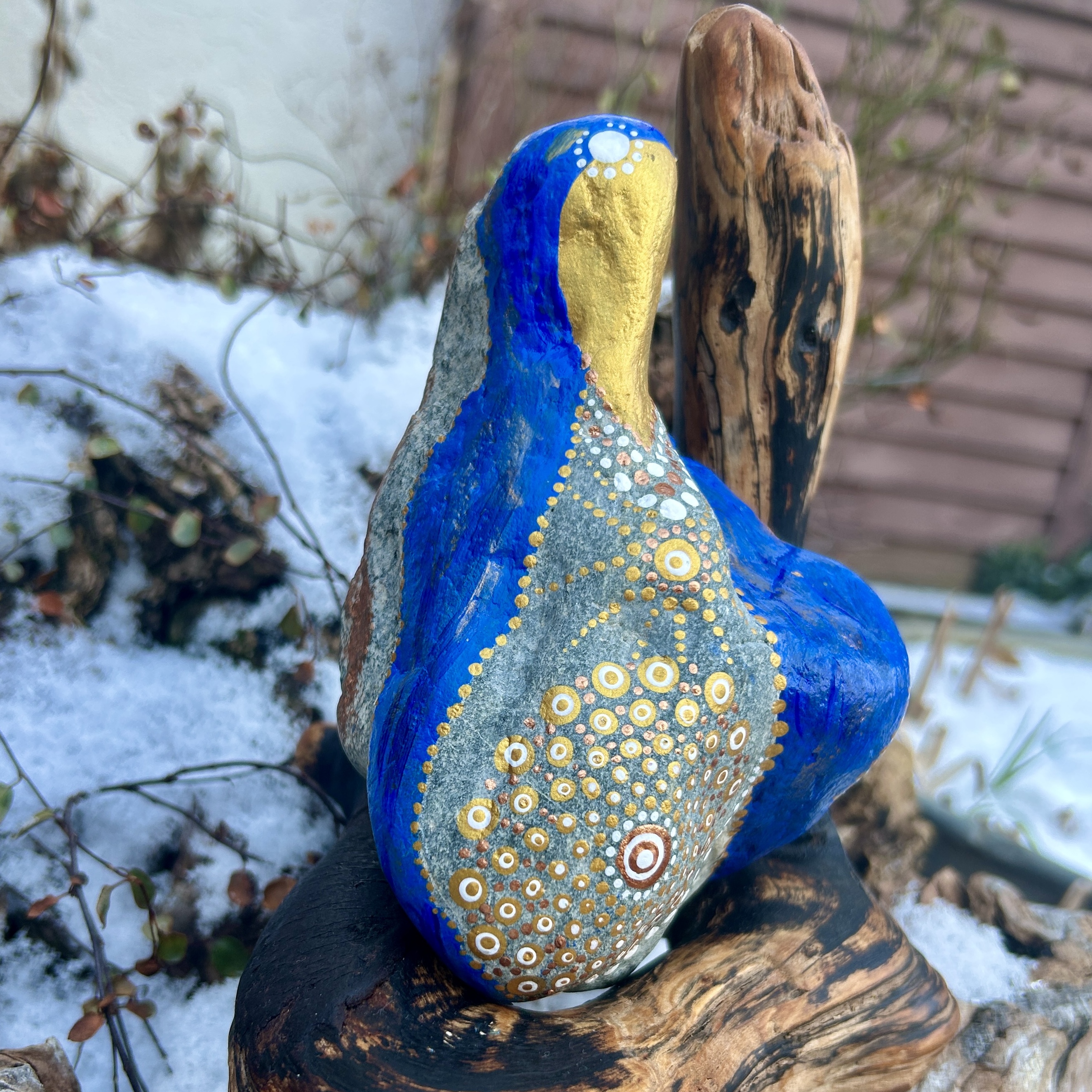 Stein in blau und gold in der Gestalt von Mutter Maria bemalt auf Treibholz stehend