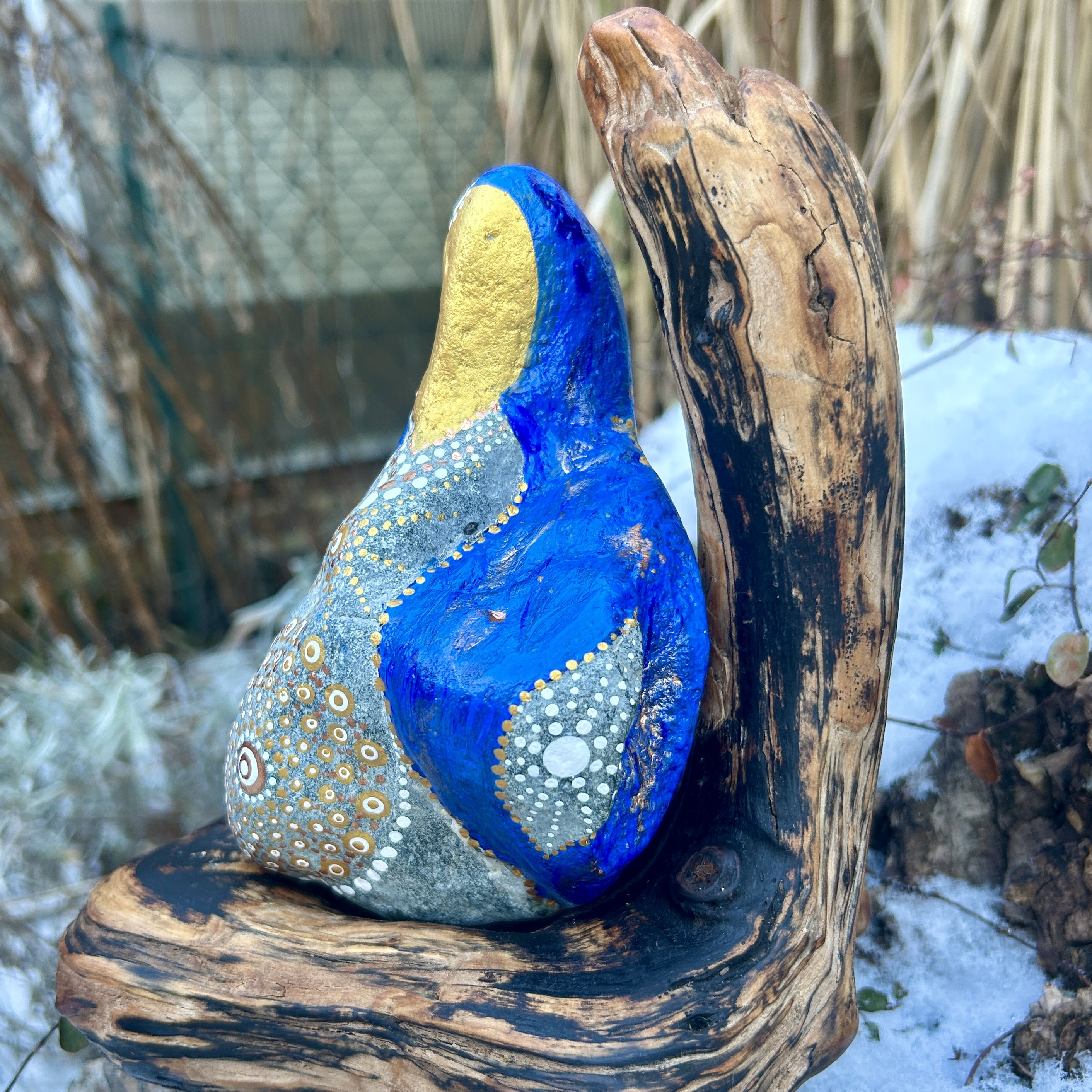 Stein in blau und gold in der Gestalt von Mutter Maria bemalt auf Treibholz stehend