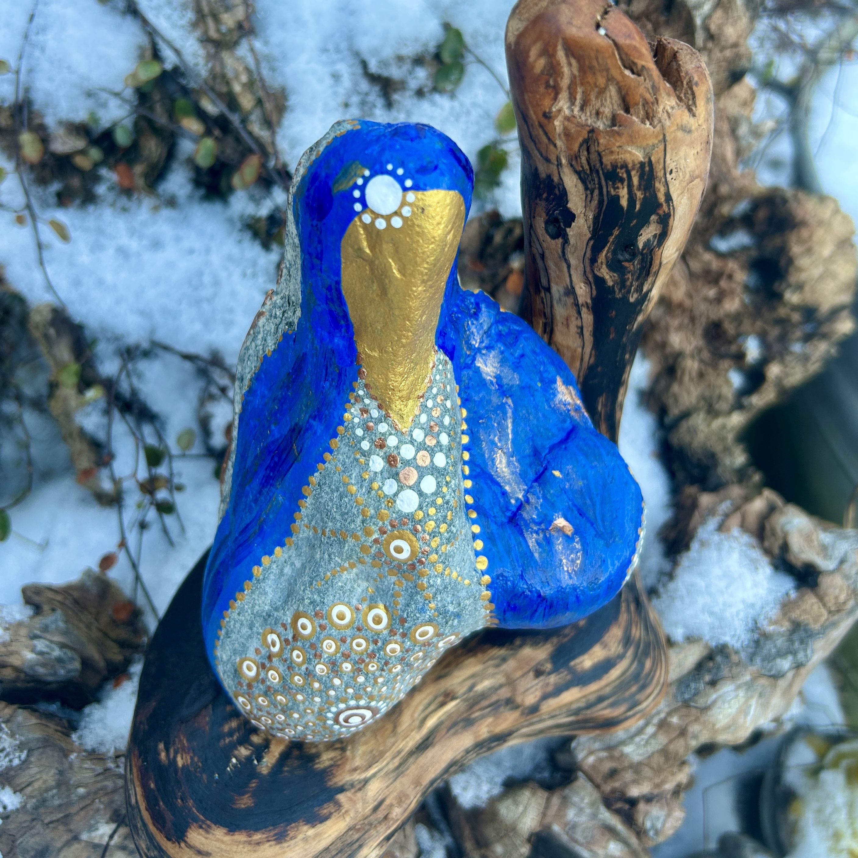 Stein in blau und gold in der Gestalt von Mutter Maria bemalt auf Treibholz stehend