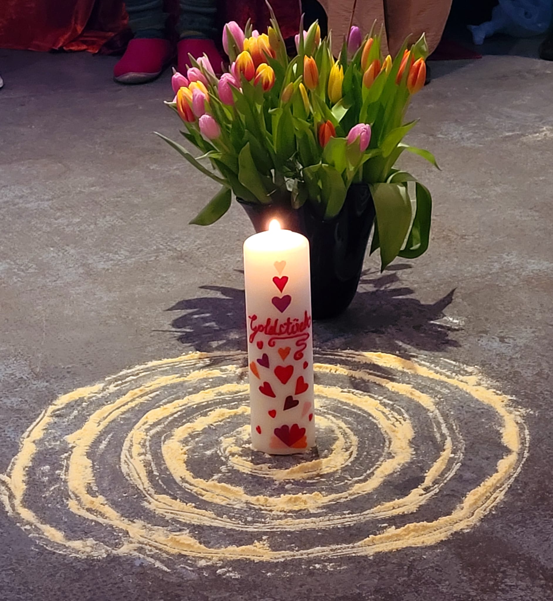 Kerze und Blumenstrauß mit Tulpen und Spirale auf Boden 
