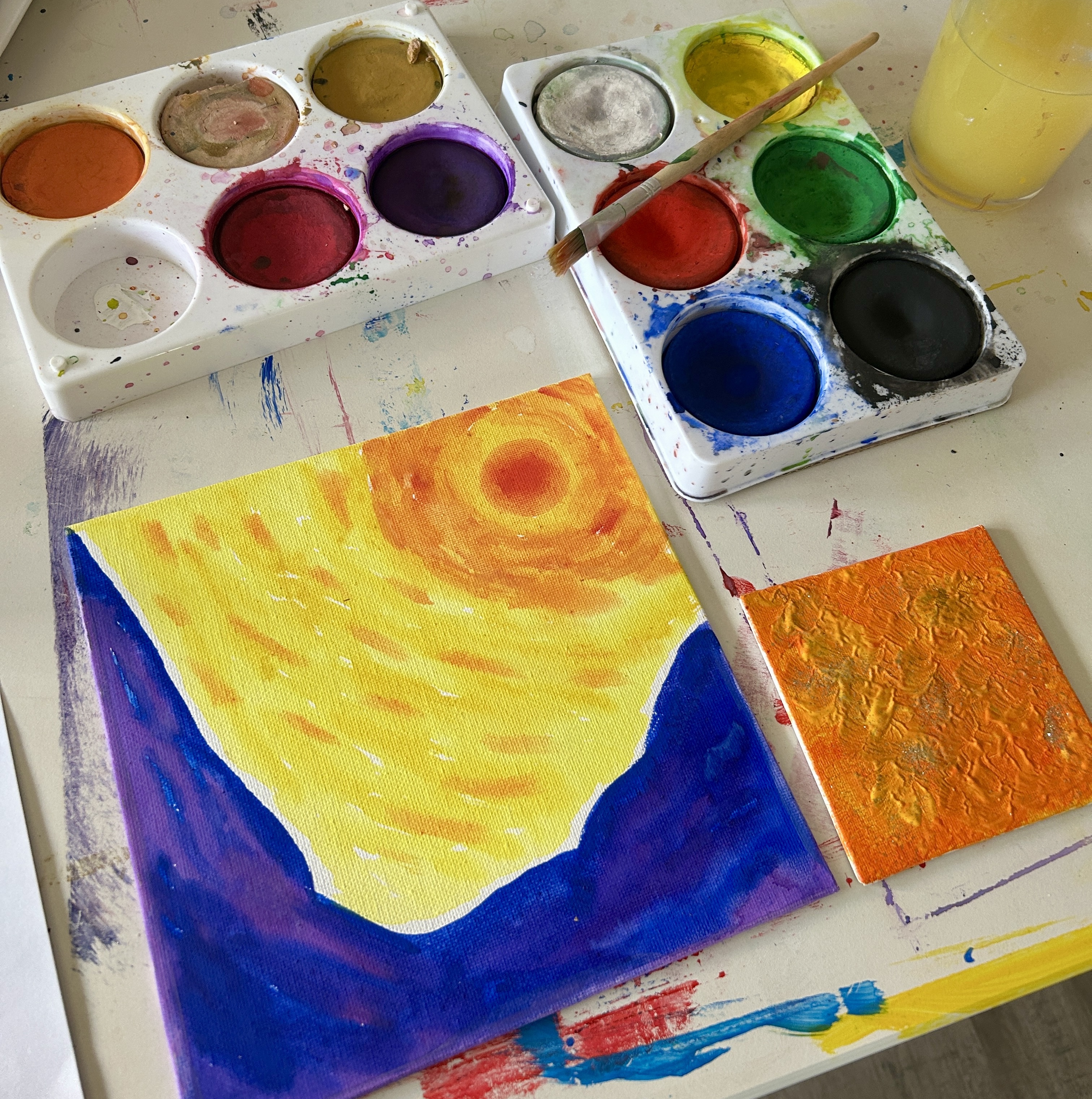 Wasserfarben und Pinsel mit zwei Bildern auf Leinwand