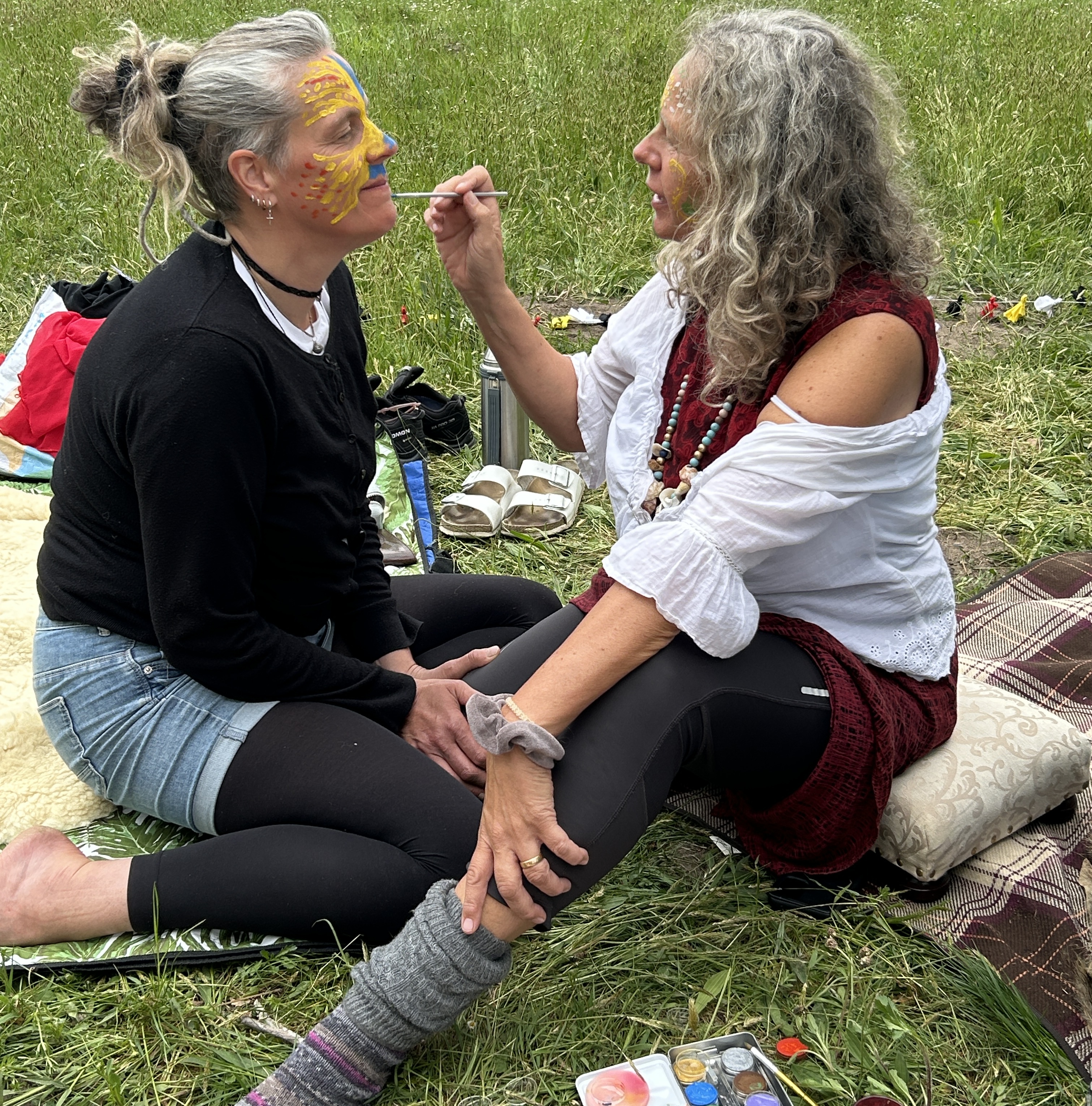 Zwei Frauen auf Boden sitzend, die einander Gesicht bemalen