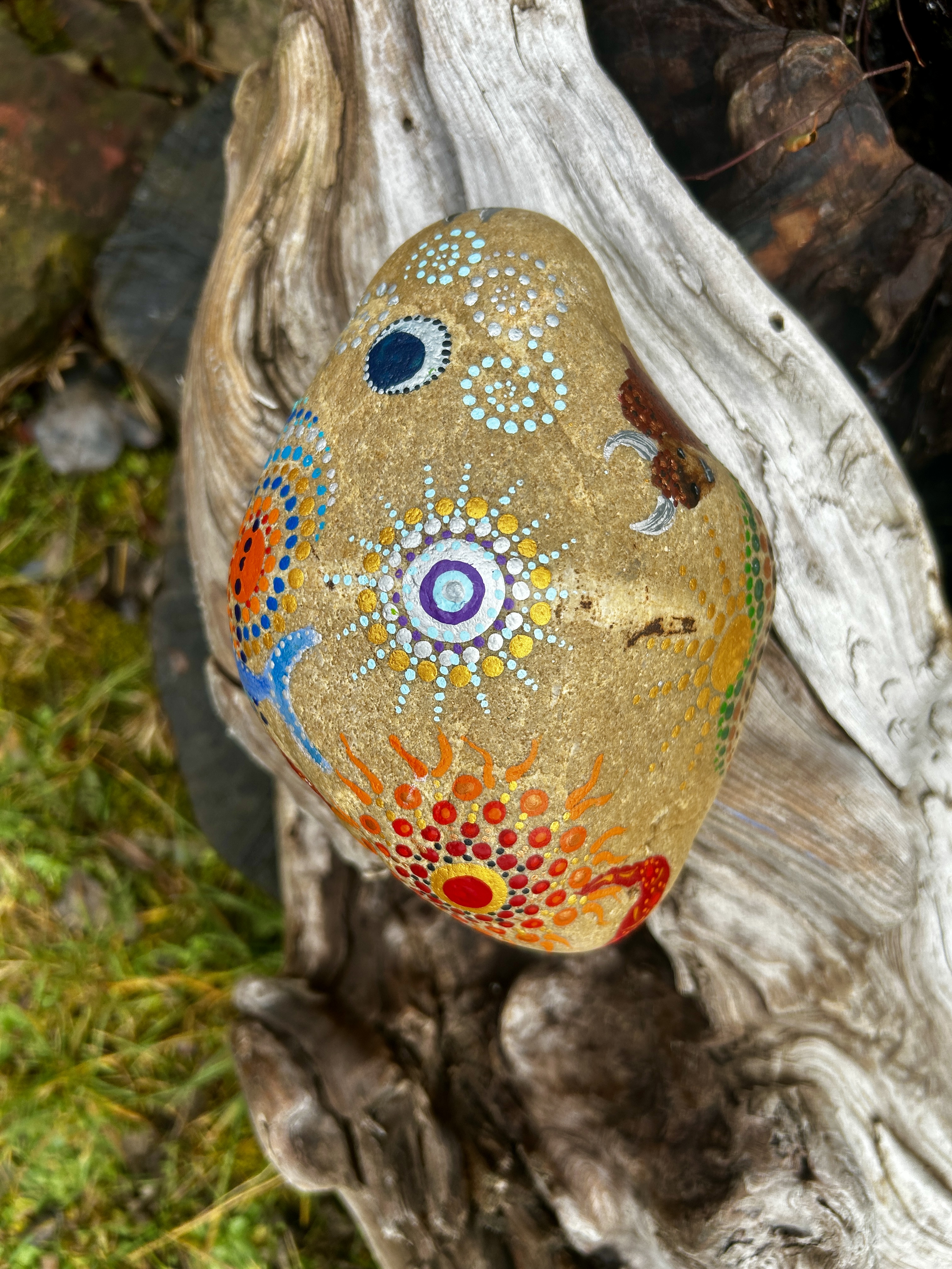 Stein in Dot Painting Technik bemalt mit Mandalas auf Wurzel liegend