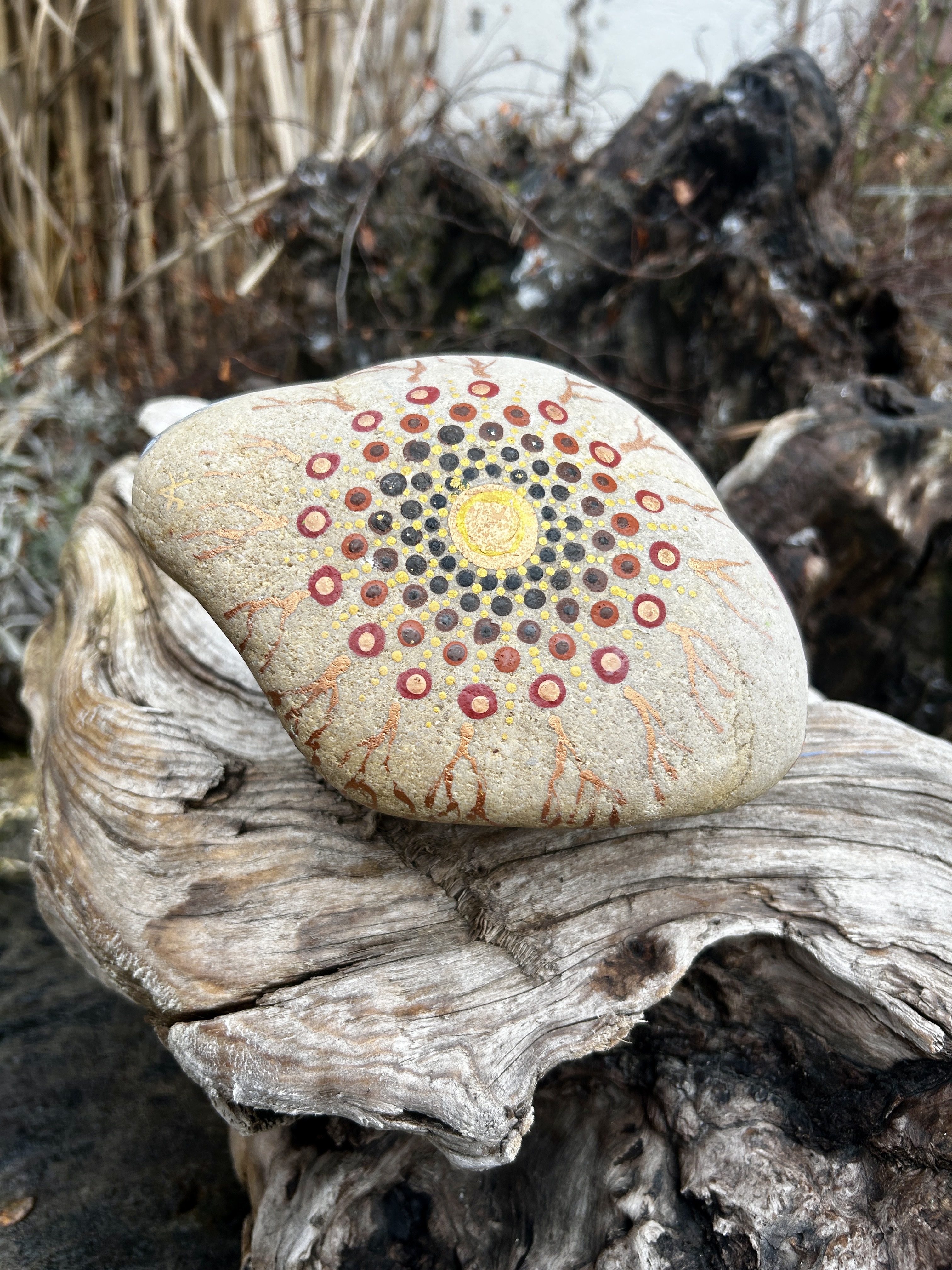 Stein in Dot Painting Technik bemalt mit Mandala auf Wurzel liegend