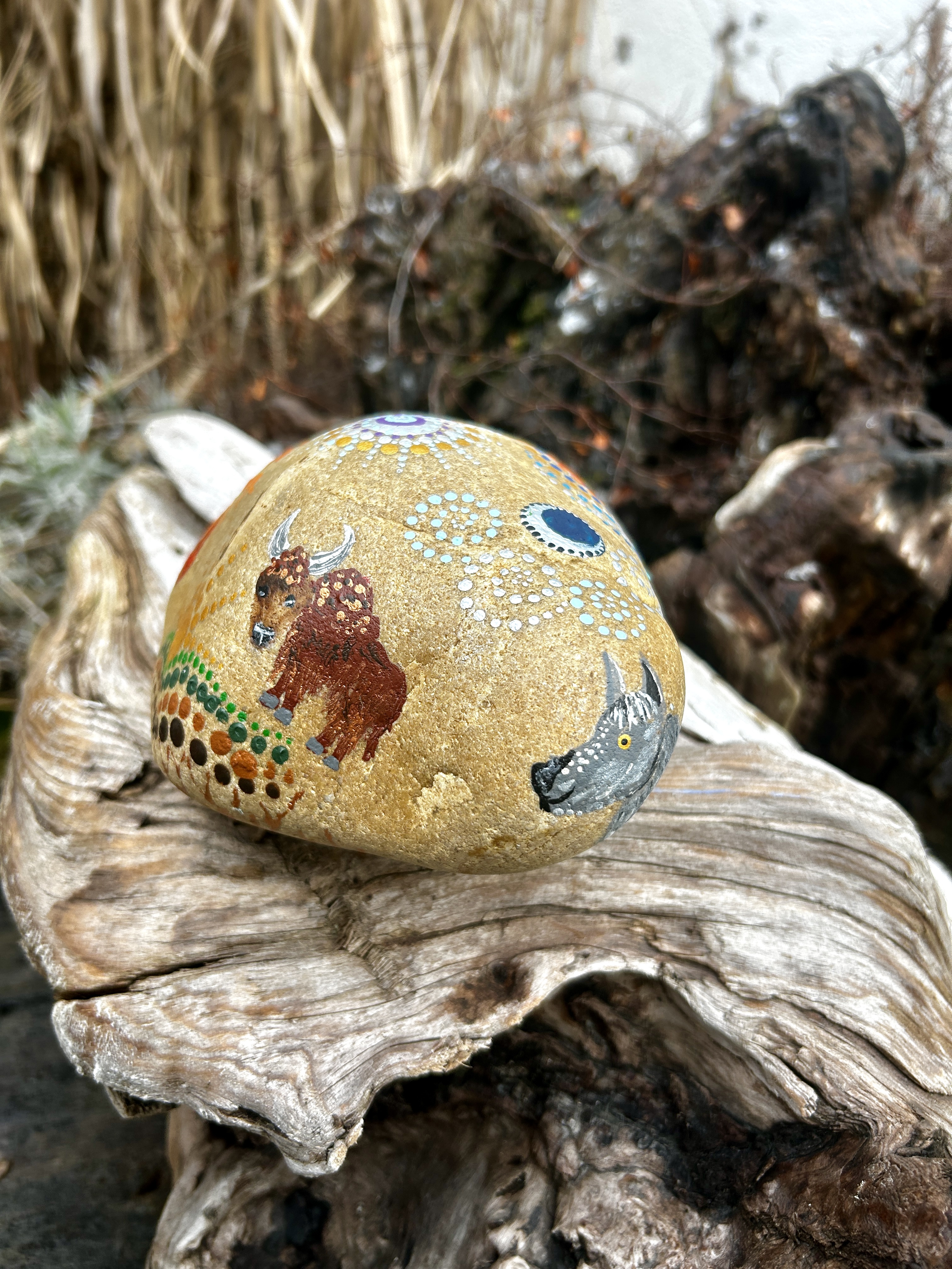 Stein in Dot Painting Technik bemalt mit Wolf und Bison auf Wurzel liegend