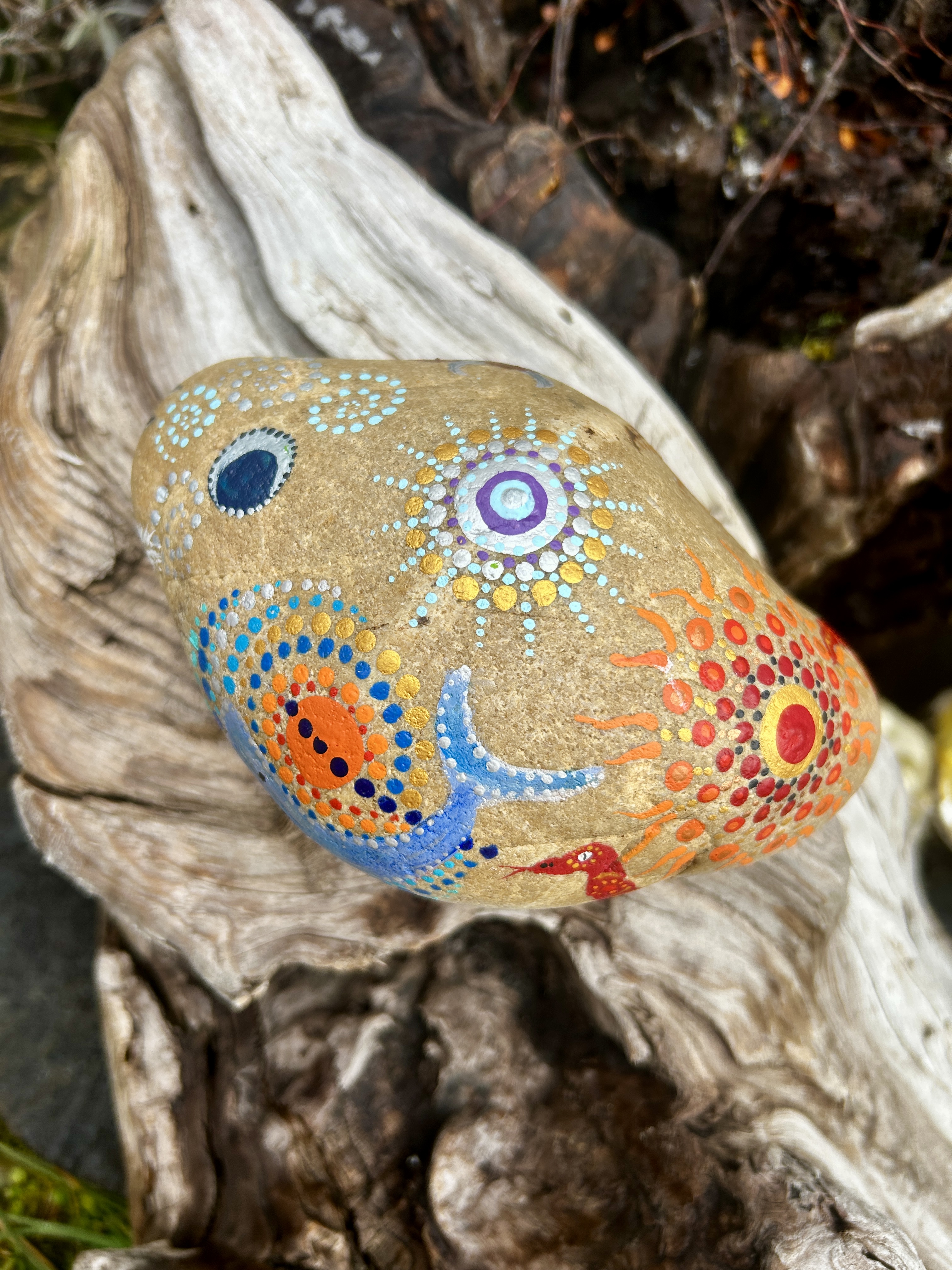 Stein in Dot Painting Technik bemalt mit Mandalas und Wal auf Wurzel liegend