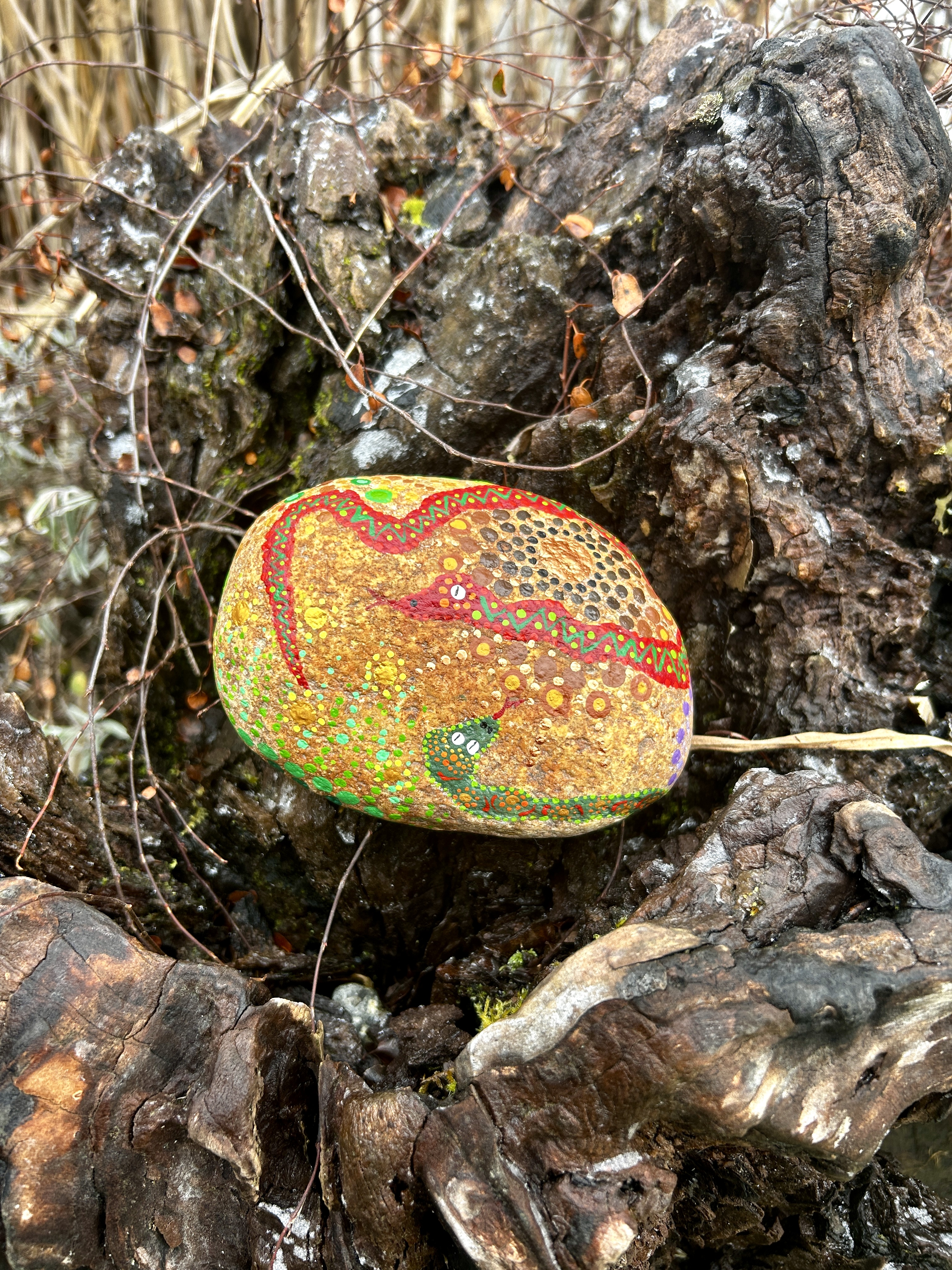 Stein in Dot Painting Technik bemalt mit Mandalas und Schlangen auf Wurzel liegend