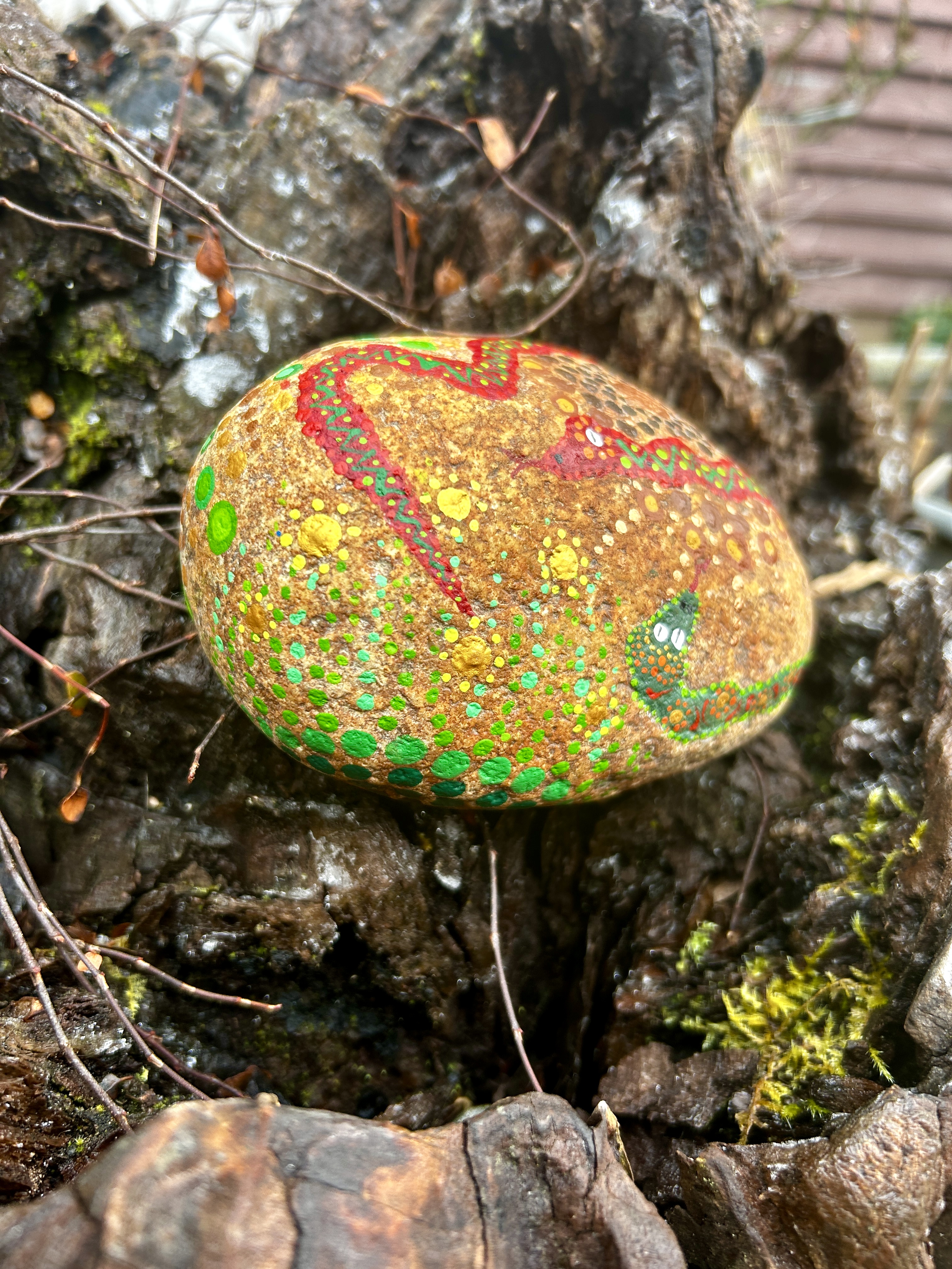 Stein in Dot Painting Technik bemalt mit SMandalas und Schlangen auf Wurzel liegend