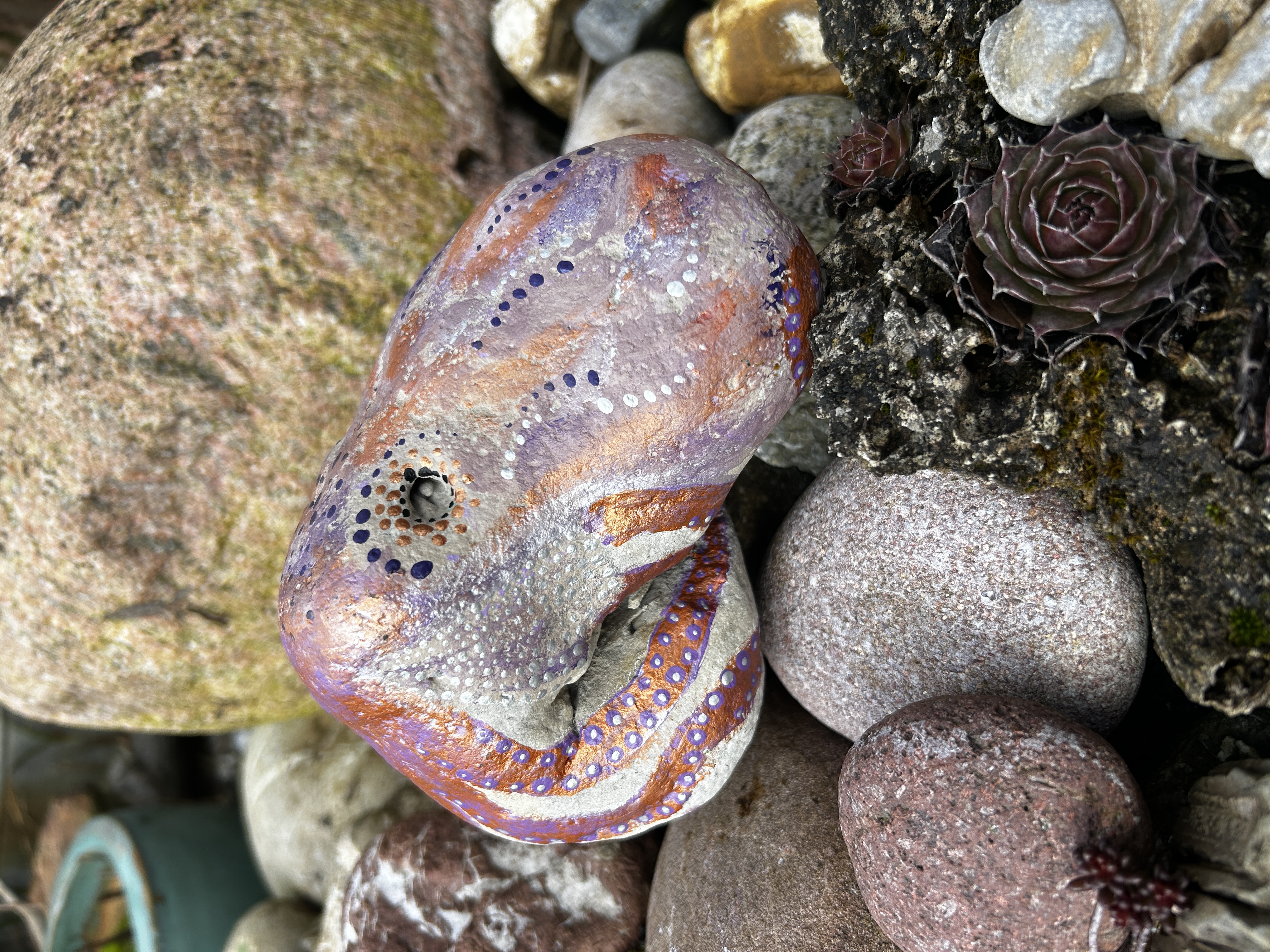 Heller Stein mit einem Oktopus bemalt auf Steinen und vor einem großen Stein liegend