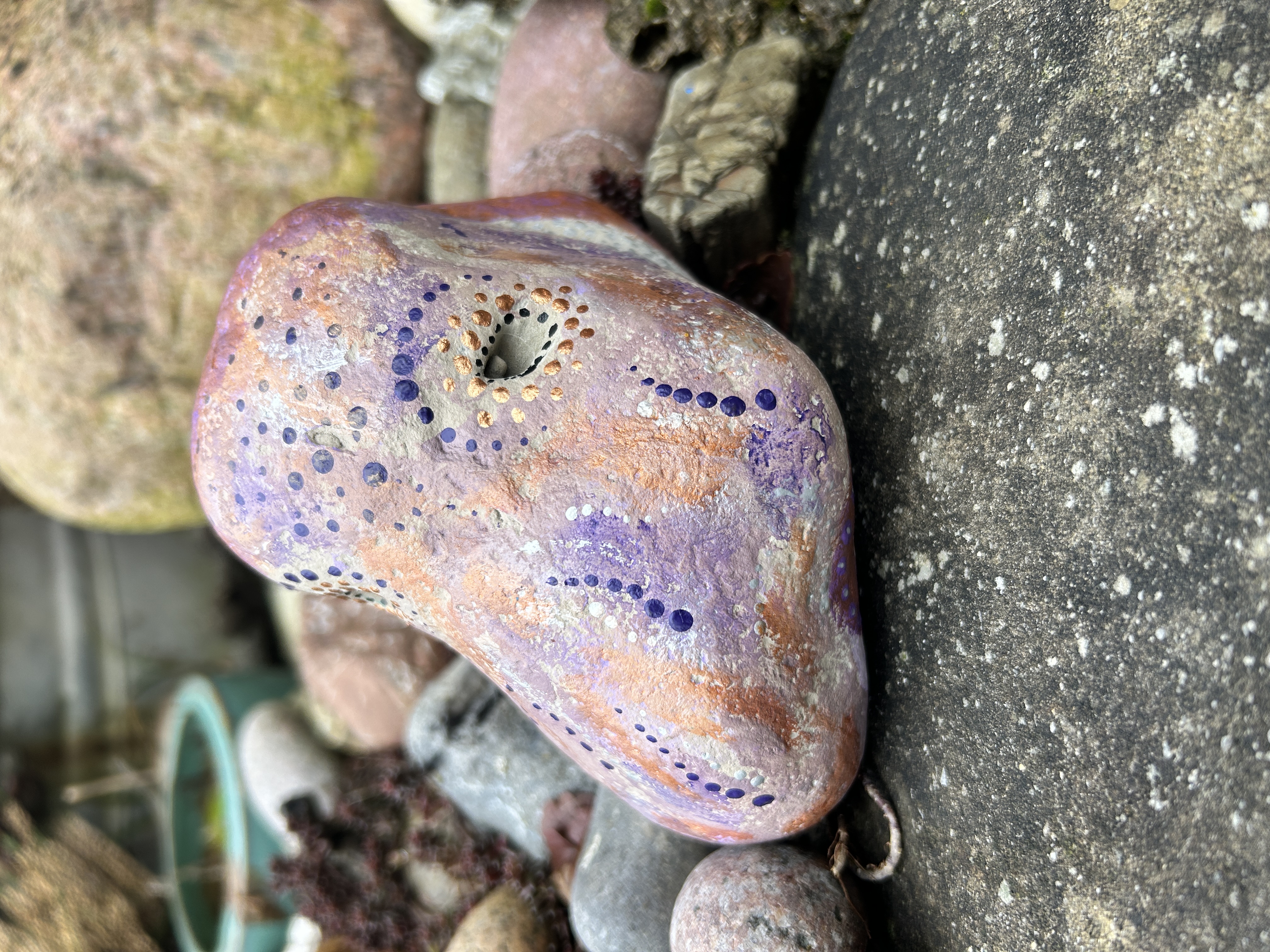 Heller Stein mit einem Oktopus bemalt auf Steinen und vor einem großen Stein liegend