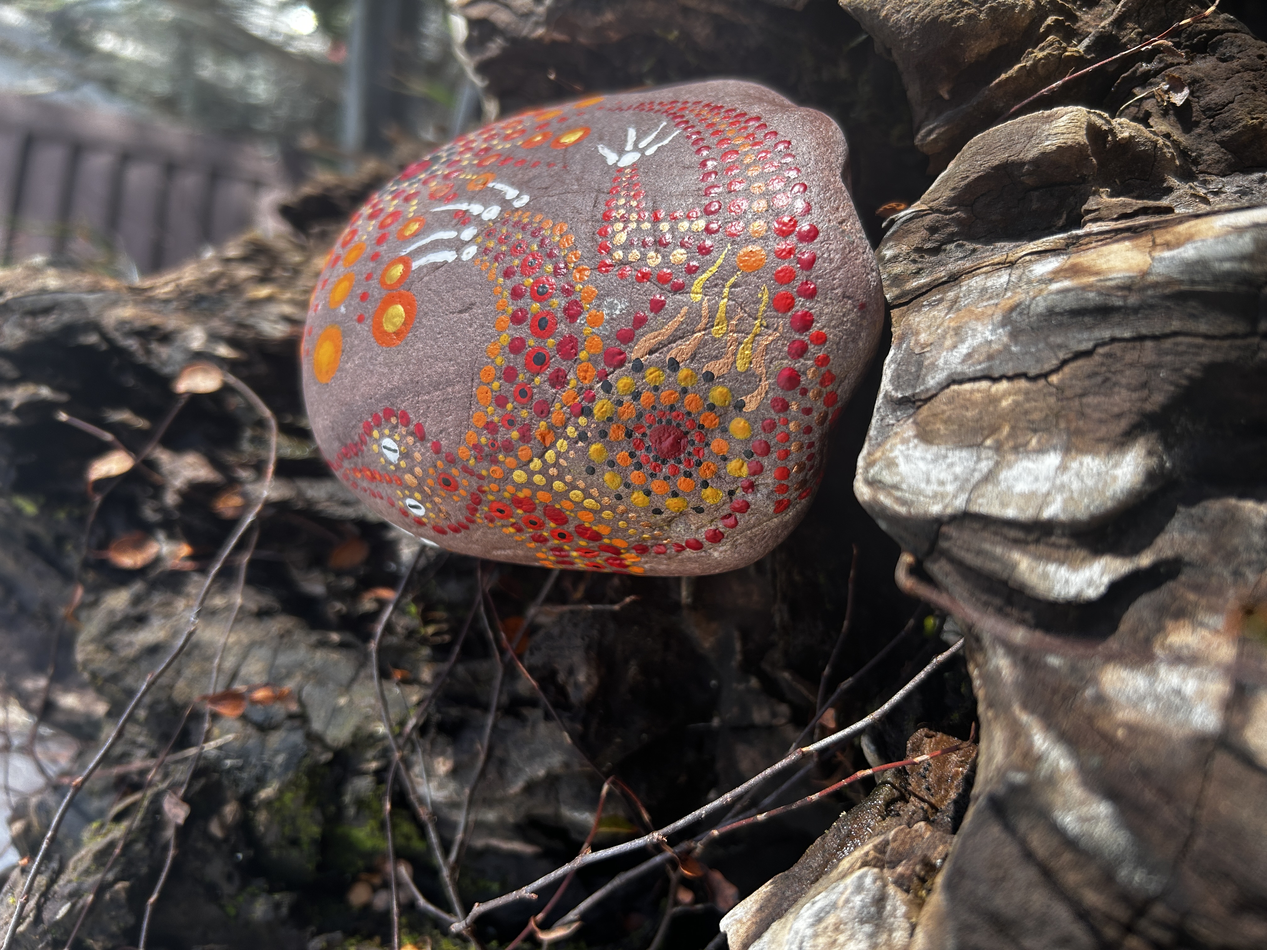 Rötlicher Stein in Dot Painting Technik  bemalt mit einem Feuerdrachen auf einer Wurzel liegend