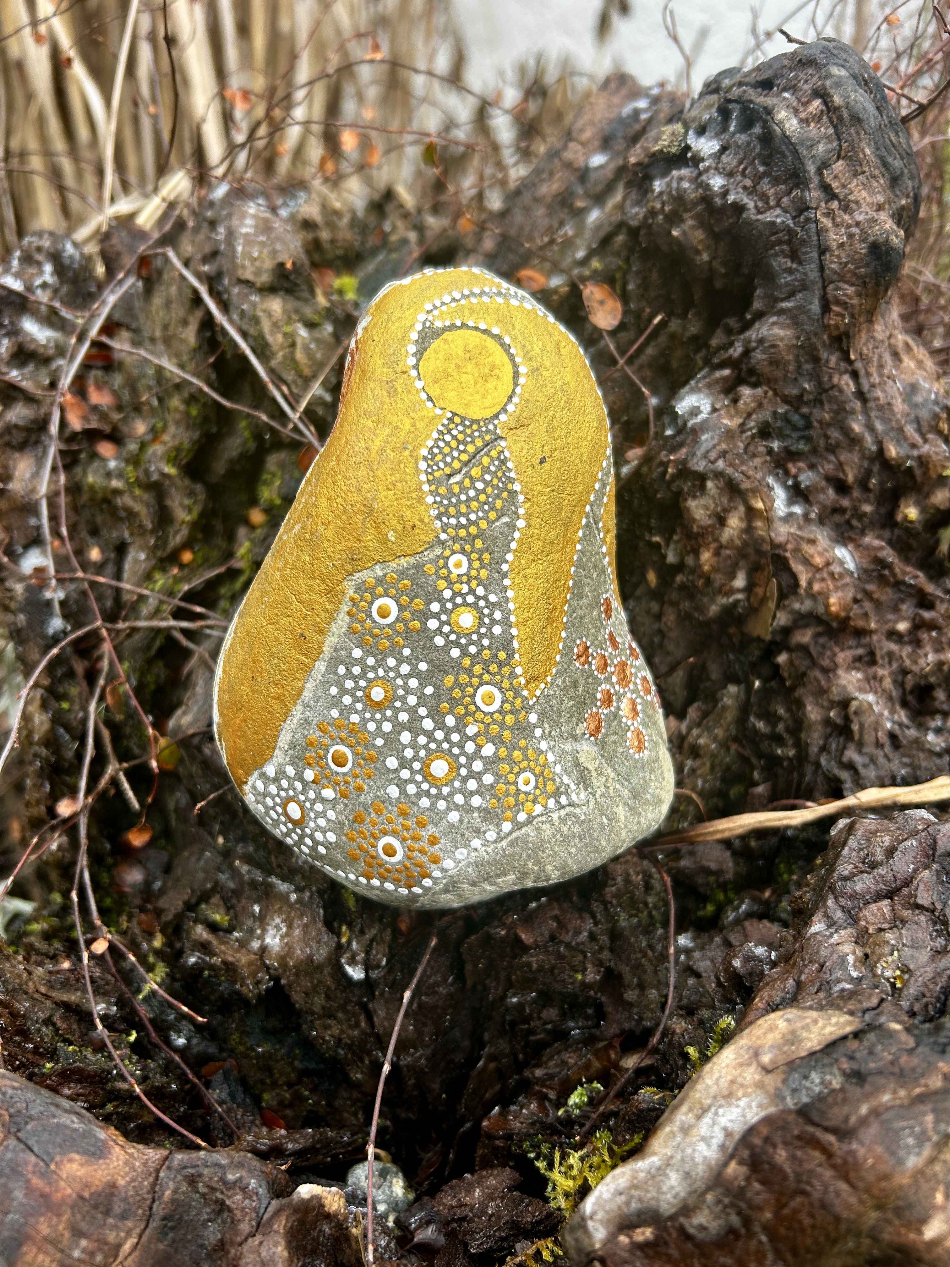 Stein mit einem Engel in Dot Painting Technik bemalt in Gold und weiß auf einer Wurzel stehend
