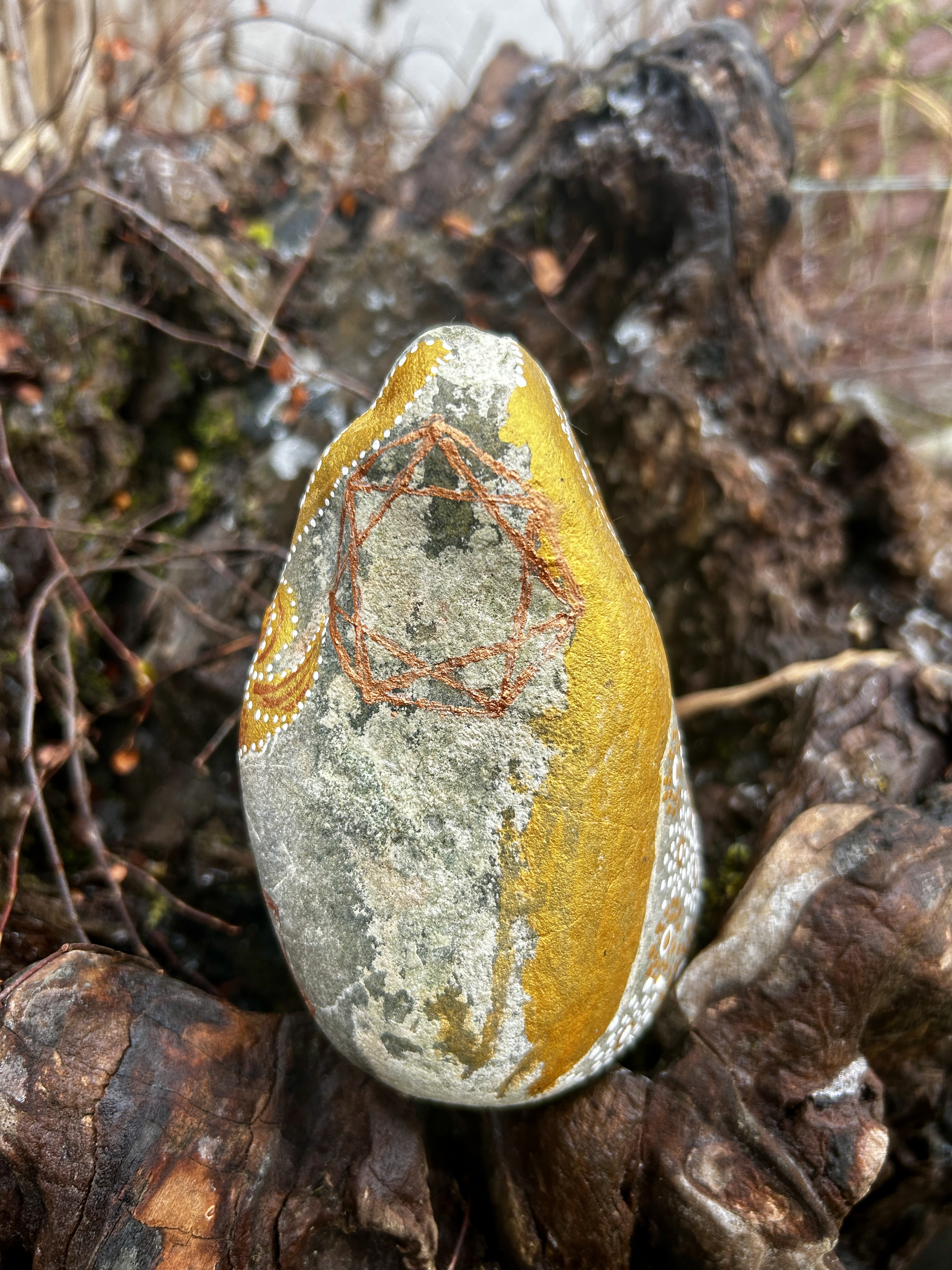 Stein mit einem Engel in Dot Painting Technik bemalt in Gold und weiß auf einer Wurzel stehend