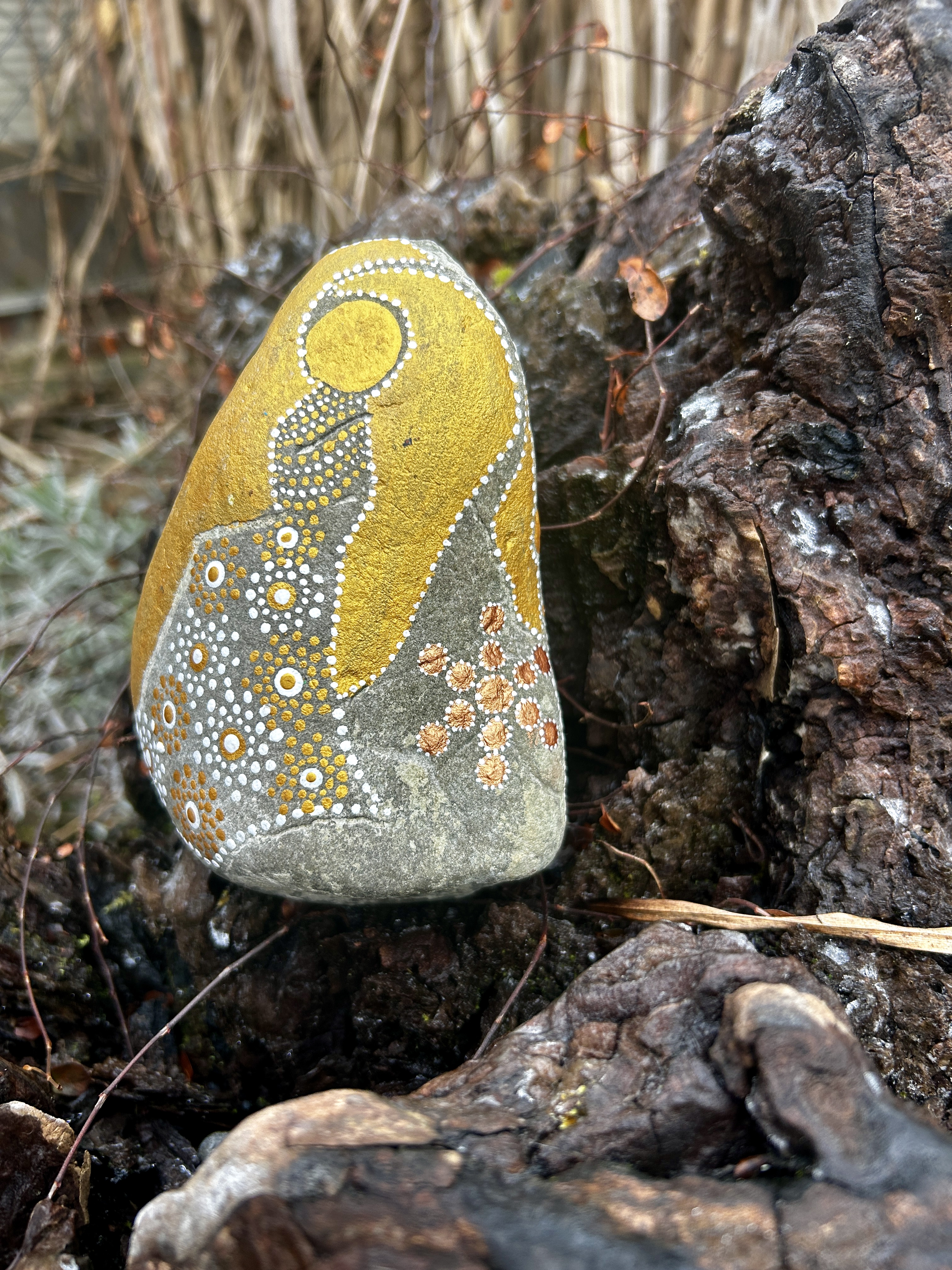 Stein mit einem Engel in Dot Painting Technik bemalt in Gold und weiß auf einer Wurzel stehend