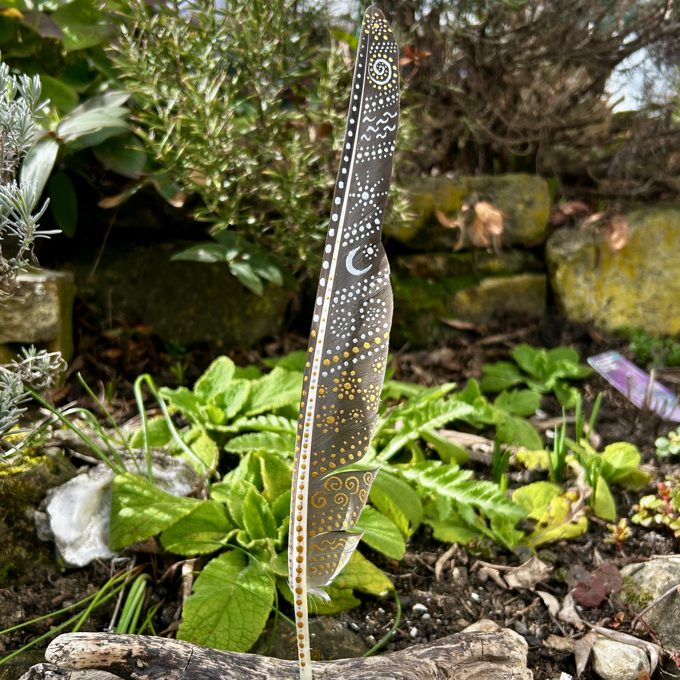 Eine bemalte Federn im Garten stehend in Silber und Gold gestaltet mit Symbolen