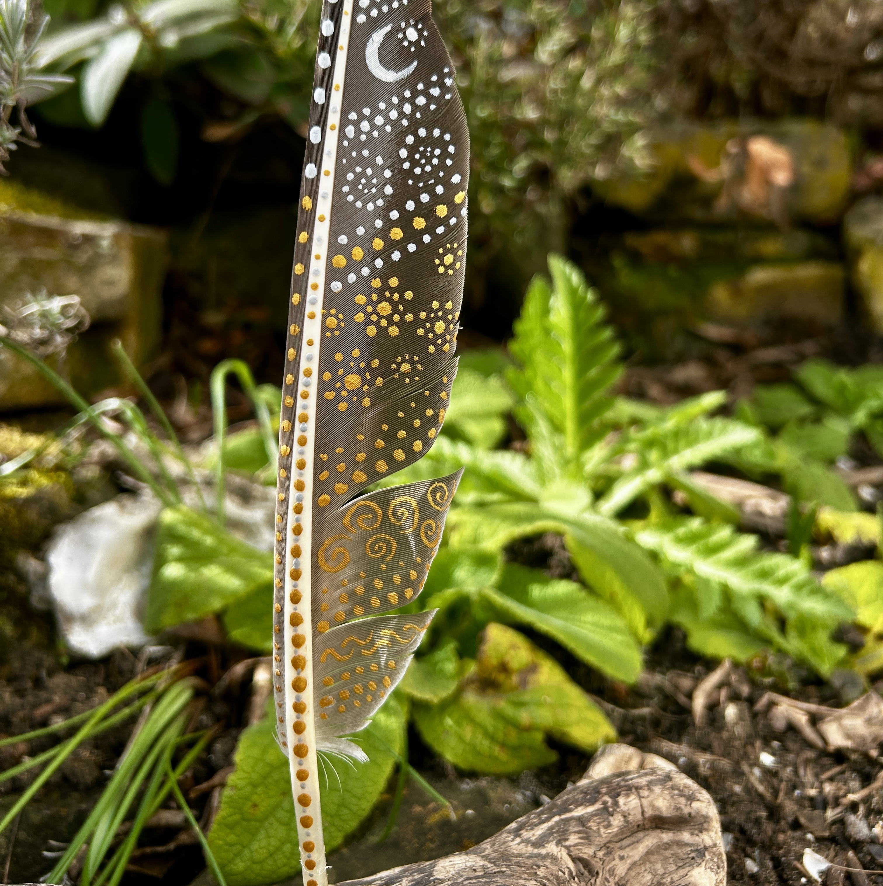 Eine bemalte Federn im Garten stehend in Silber und Gold gestaltet mit Symbolen