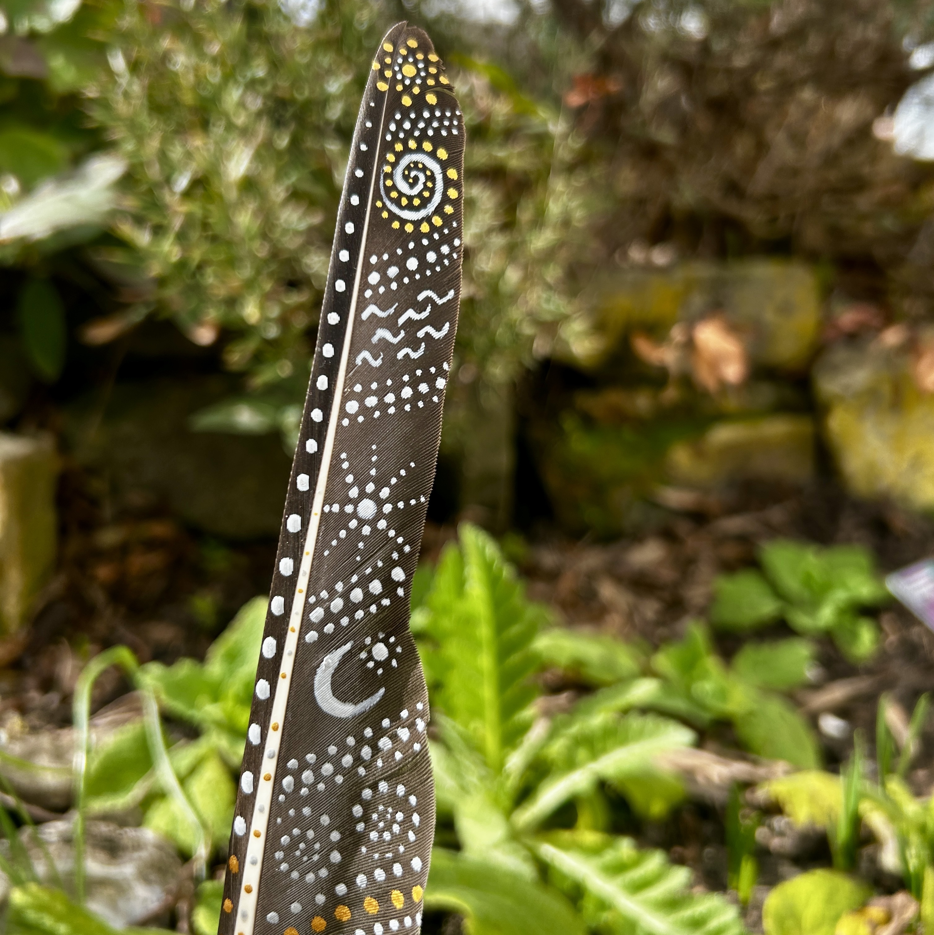 Eine bemalte Federn im Garten stehend in Silber und Gold gestaltet mit Symbolen