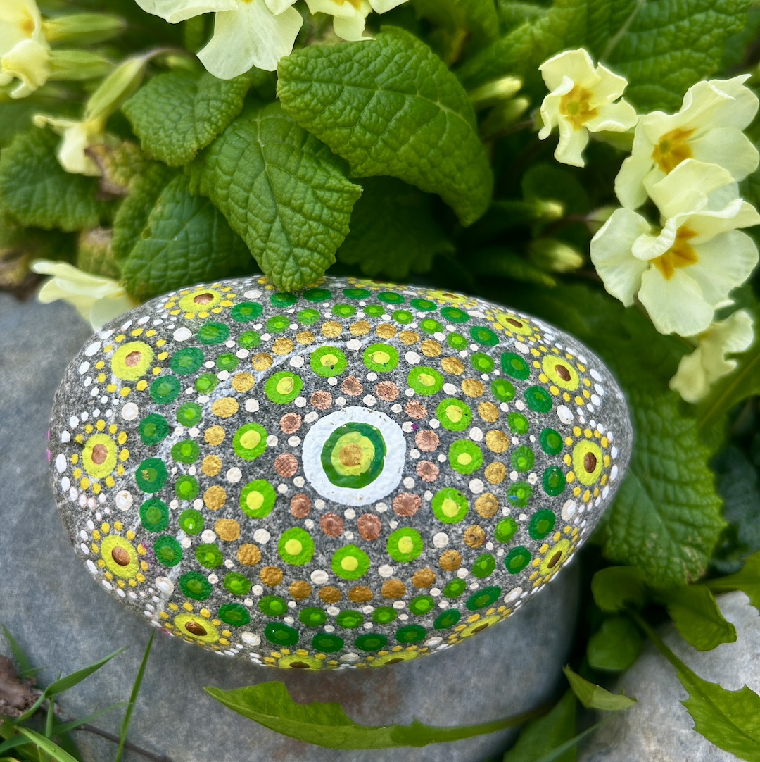 In Dot painting Technik bemalter Stein mit einem Mandala in Grün und Gelbtönen vor Primeln