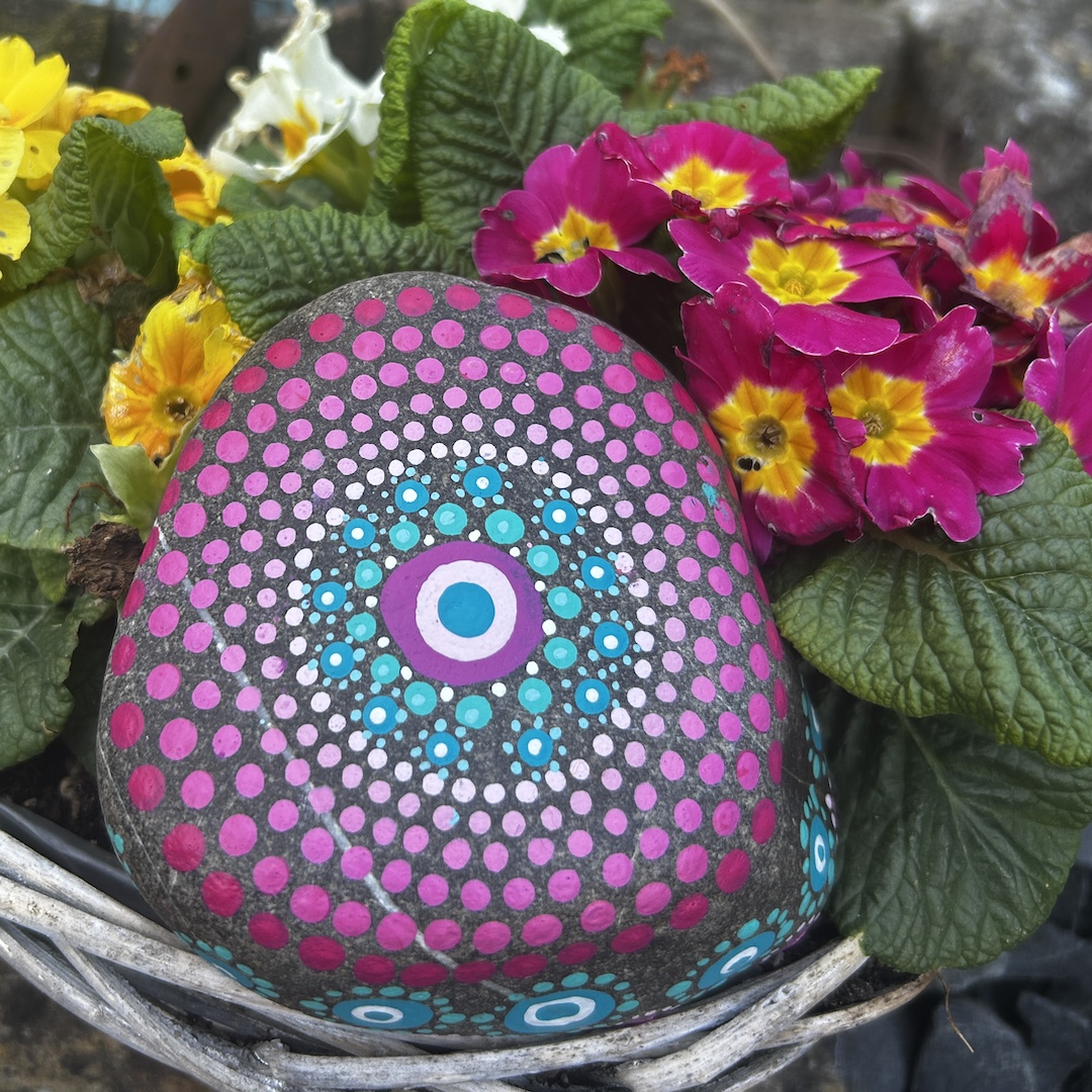 In Dot painting Technik bemalter Stein mit einem Mandala in Rosa- undTürkistönen vor Primeln