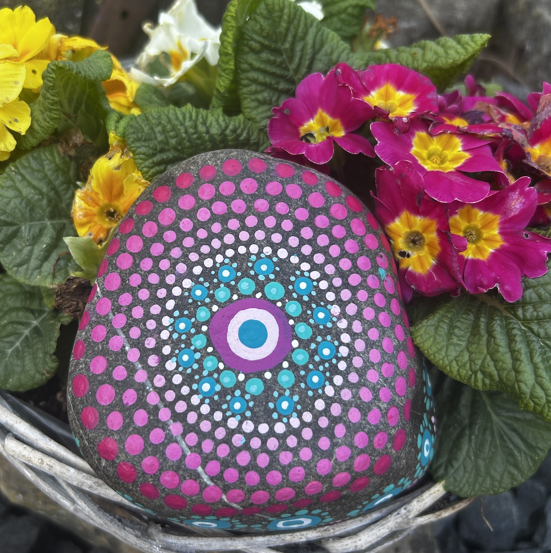 In Dot painting Technik bemalter Stein mit einem Mandala in Rosa- und Türkistönen vor Primeln