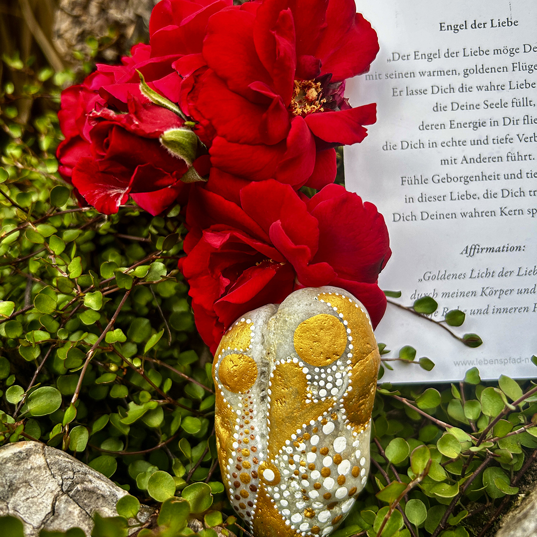 Stein mit zwei Engeln bemalt vor roten Rosen liegend