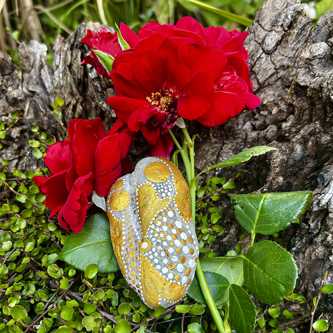 Stein mit zwei Engeln bemalt vor roten Rosen liegend