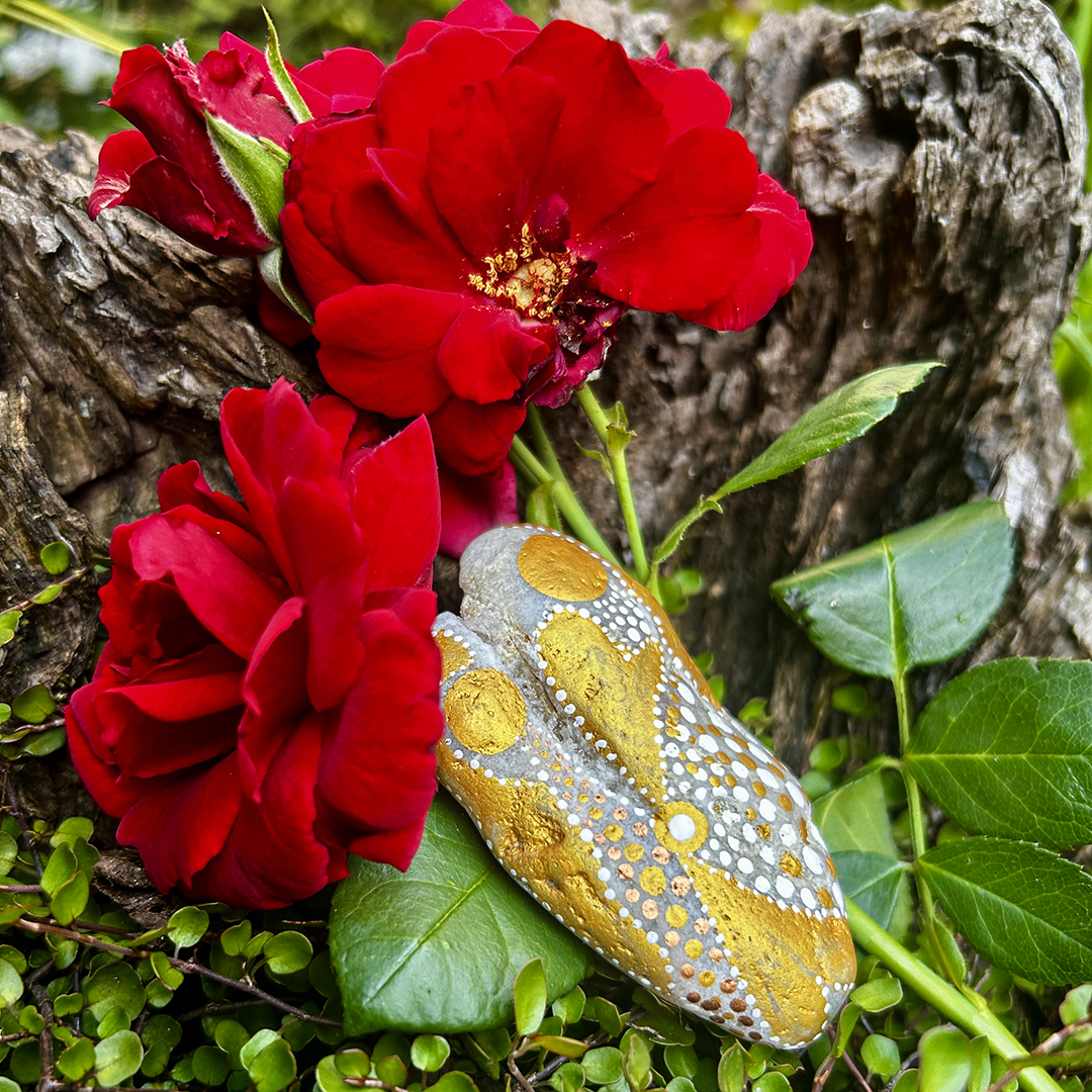 Stein mit zwei Engeln bemalt vor roten Rosen liegend