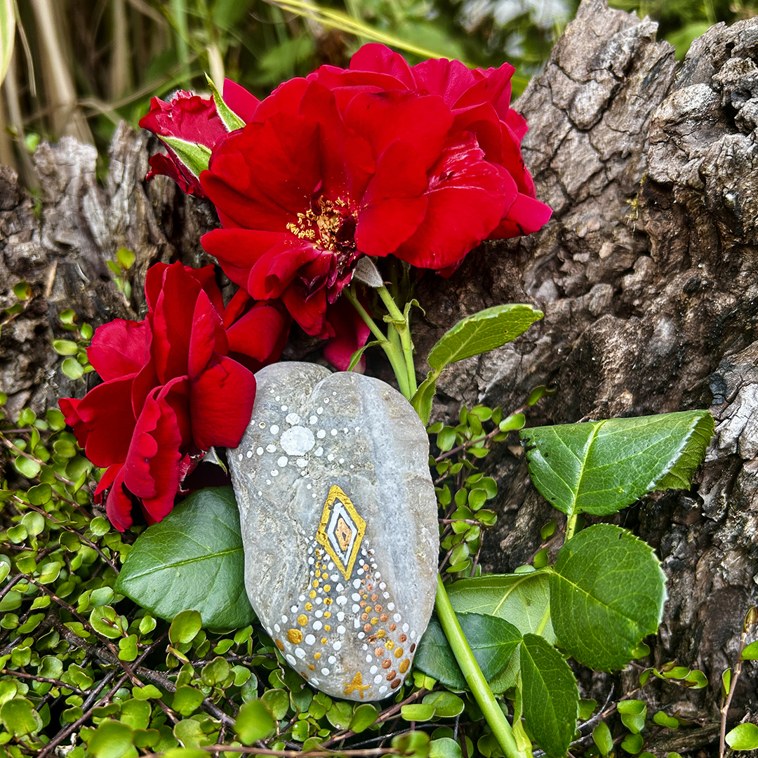 Stein mit zwei Engeln bemalt vor roten Rosen liegend