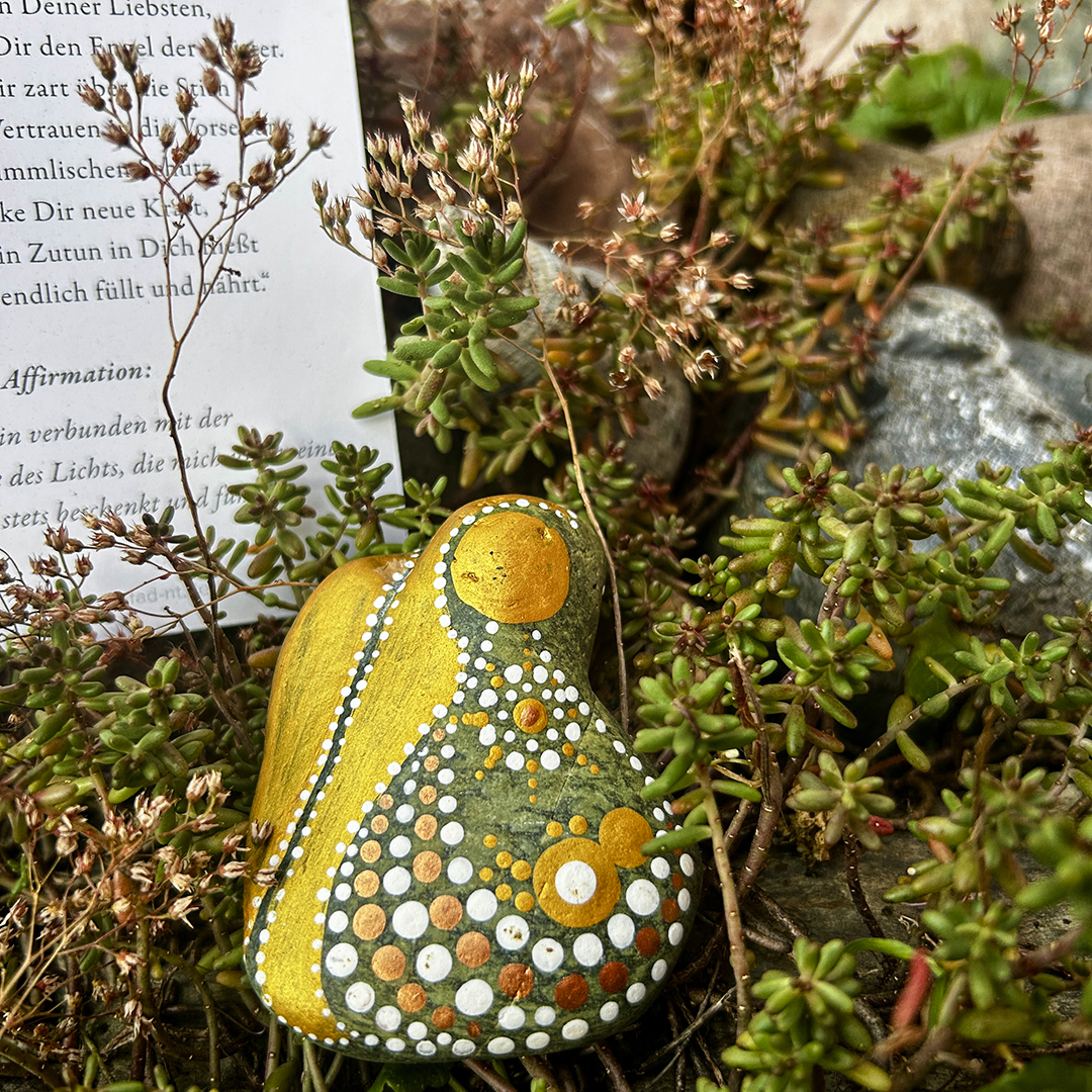Ein Stein mit einem Engel bemalt auf Grünpflanzen liegend