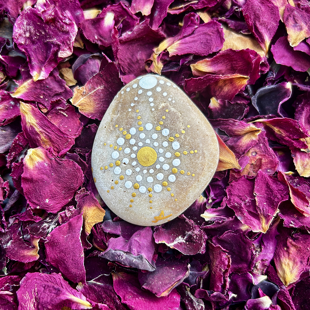 Bemalter Stein mit Mandala in gold und weiß auf Rosenblätter