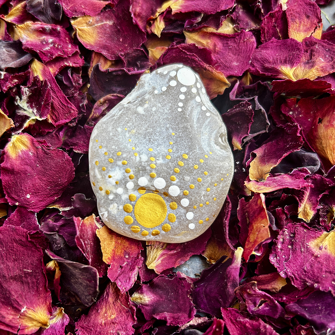 Bemalter Stein mit aufgehender Sonne auf Rosenblätter