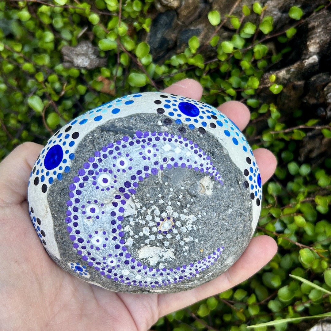 Grau- weißer Stein mit einem Mond und Stern in Dot Painting Technik bemalt in der Hand gehalten