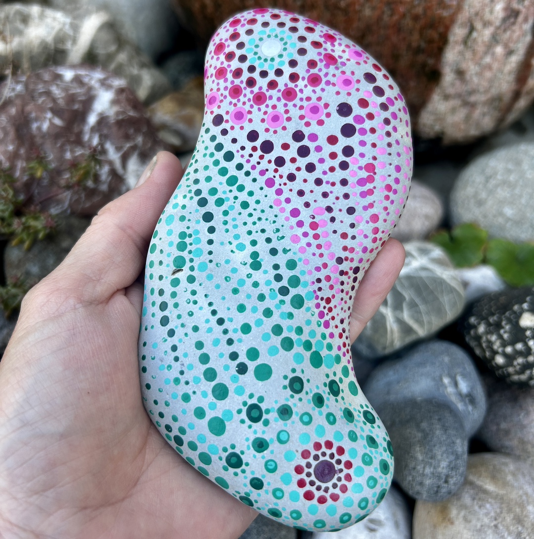 Stein mit einem mintfarbenen und magentafarbenen Mandala in Dot Painting technik bemalt in der Hand gehalten