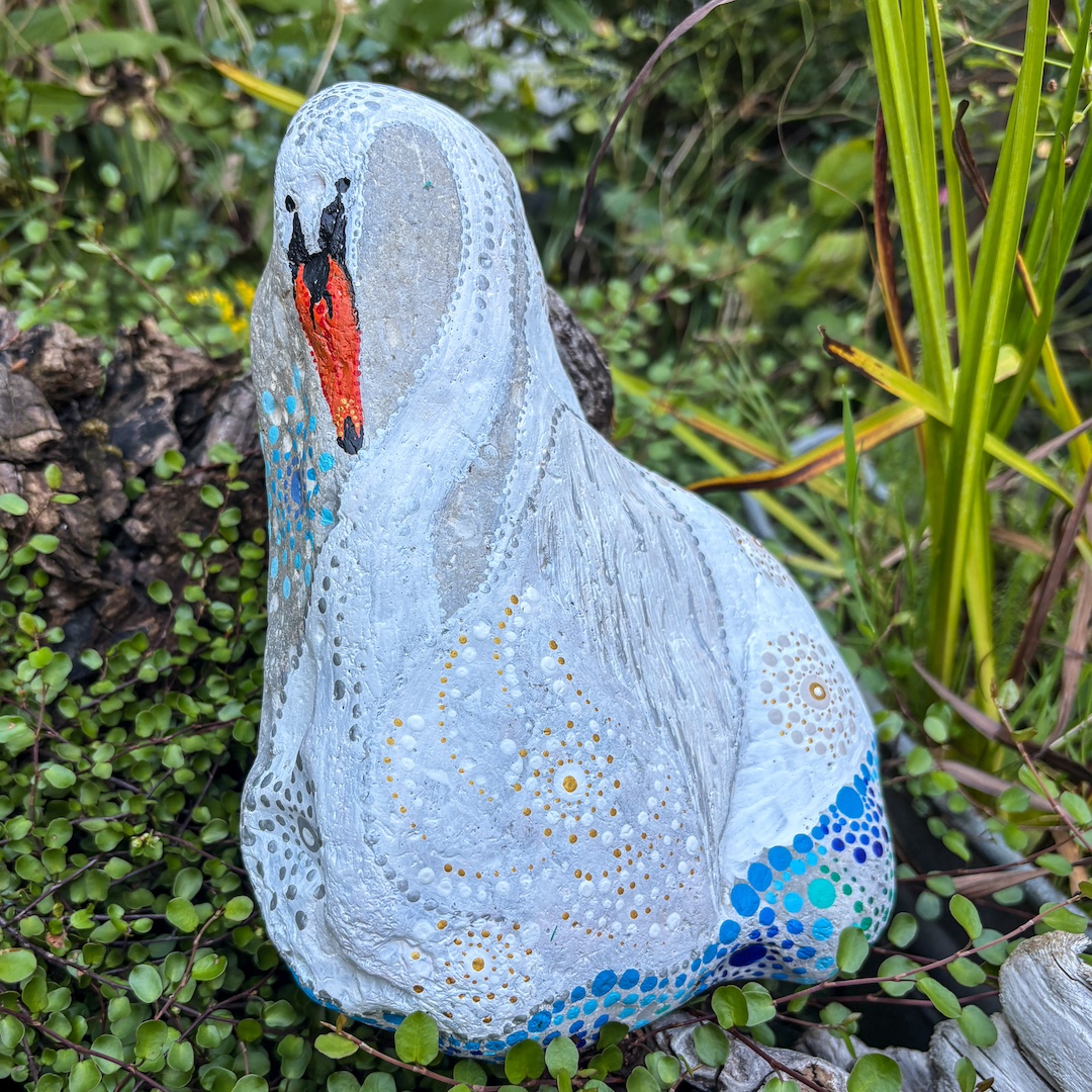 Heller Stein mit einem Schwan bemalt auf Pflanzen liegend