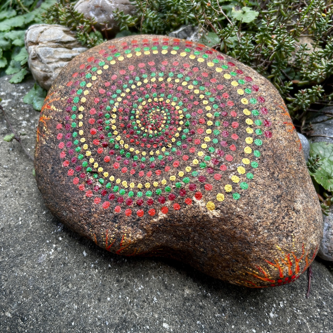 Ein rötlicher Stein mit gemalter Spirale in rot, grün und Gold