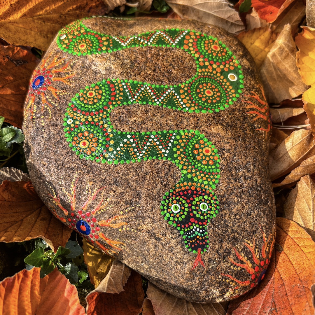 Ein rötlicher Stein mit Schlange in Grüntönen gestaltet auf Herbstlaub liegend