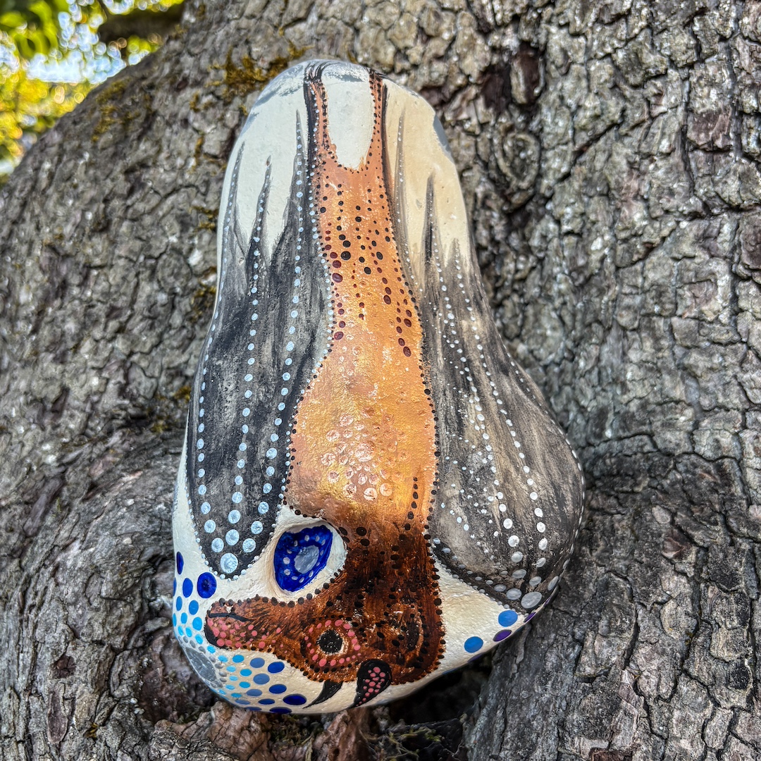Stein mit hängendem Flughund bemalt vor Baumrinde