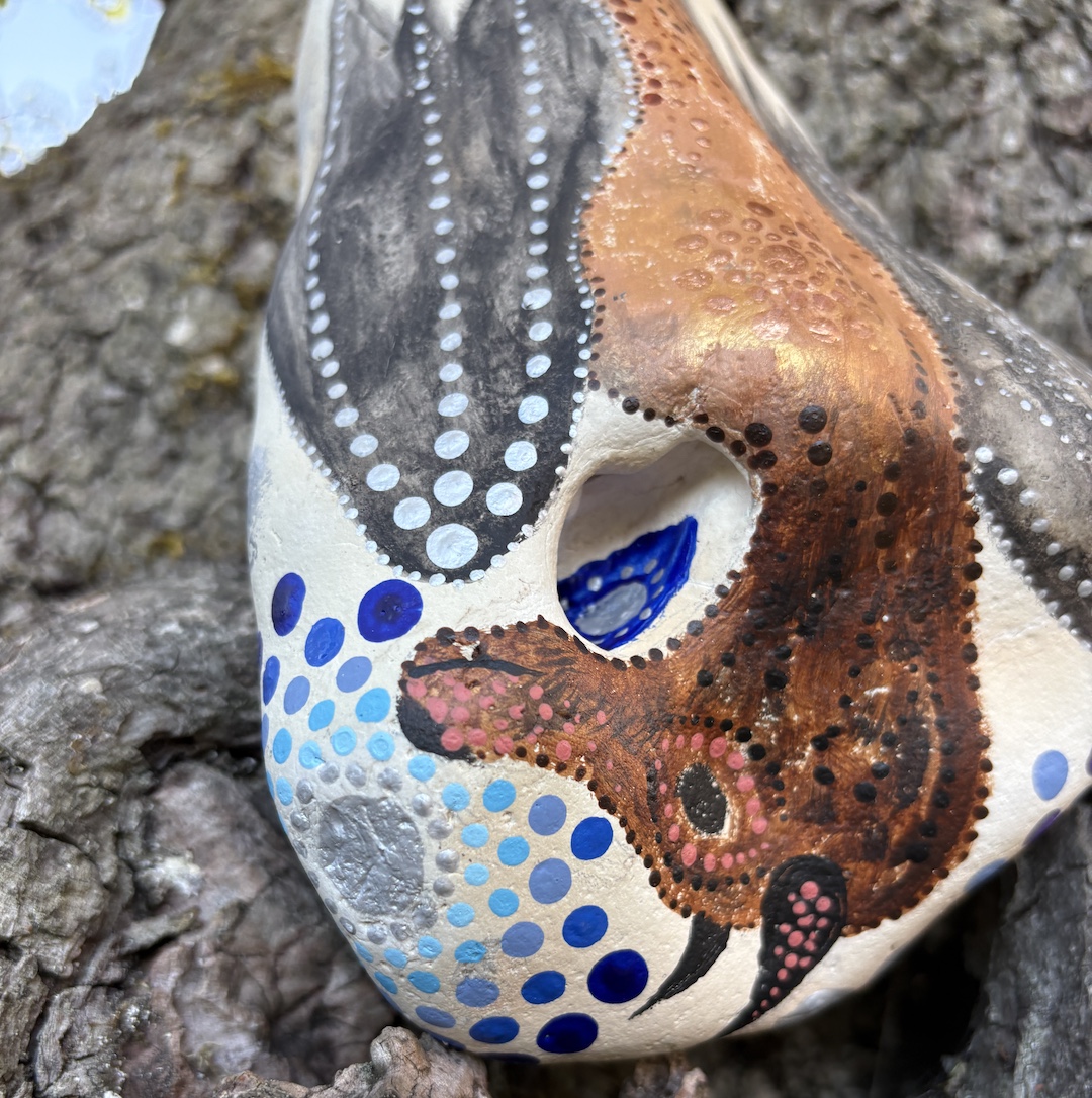 Stein mit hängendem Flughund bemalt Kopf im Detail vor Baumrinde