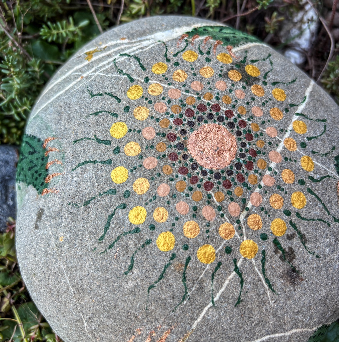 Stein mit Mandala in erdfarben bemalt auf Grünpflanzen liegend
