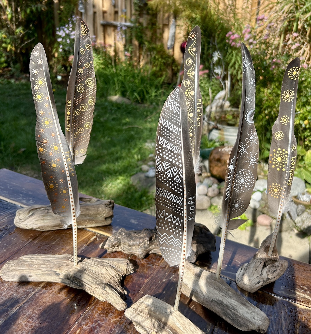 Fünf bemalte Federn auf einem Tisch im Garten stehend in Holzständern