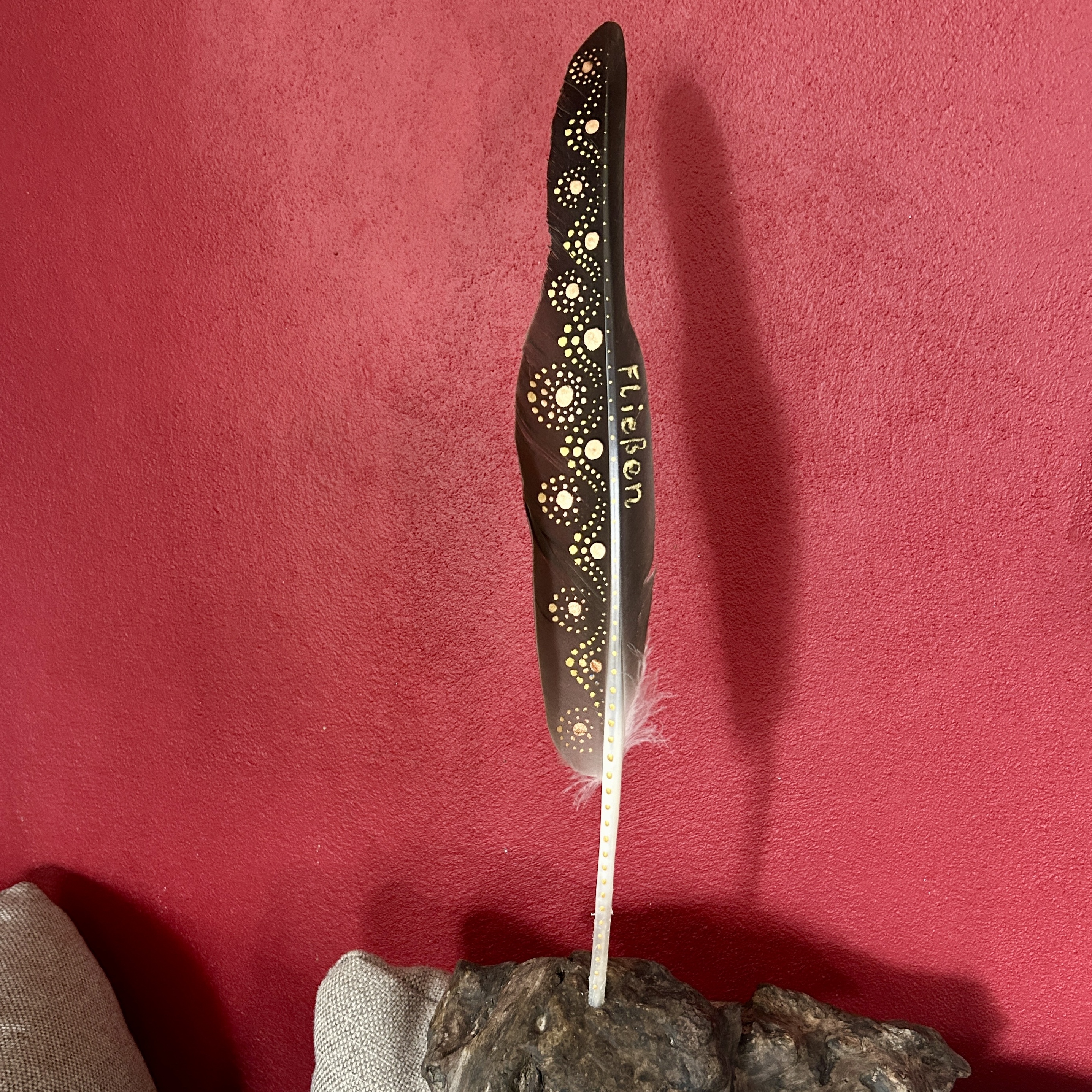 In Gold bemalte Feder vor roter Wand